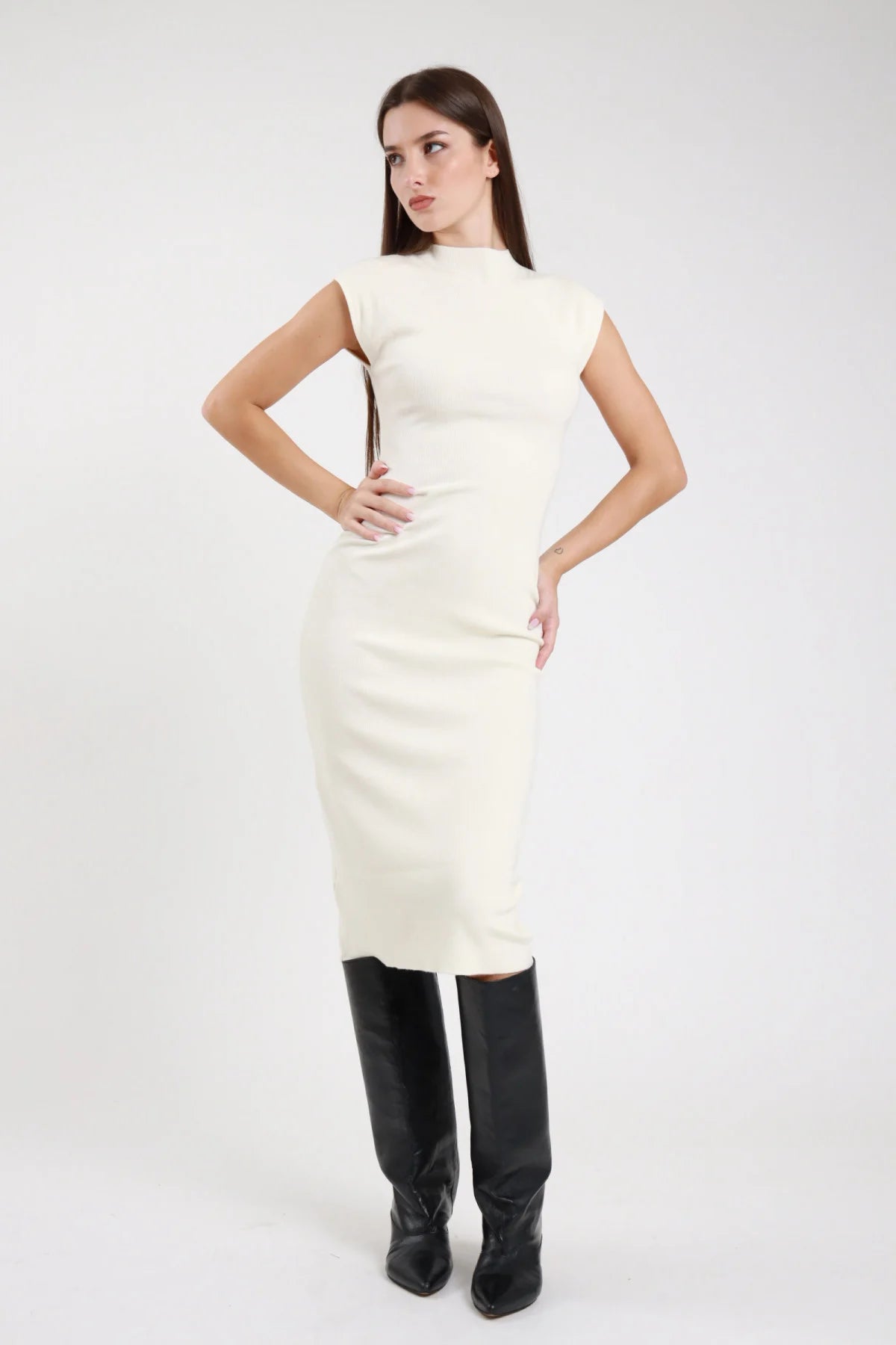 Abito tubino smanicato panna ecru off-white maglia jersey costolato frontale tre quarti mano capello collo mock neck dolcevita spallina cap sleeve corpo aderente slim fit midi spacco laterale stivali neri al ginocchio - modella frontale tre quarti mano capello sguardo laterale intenso stivali neri al ginocchio capelli castani lisci sfondo bianco