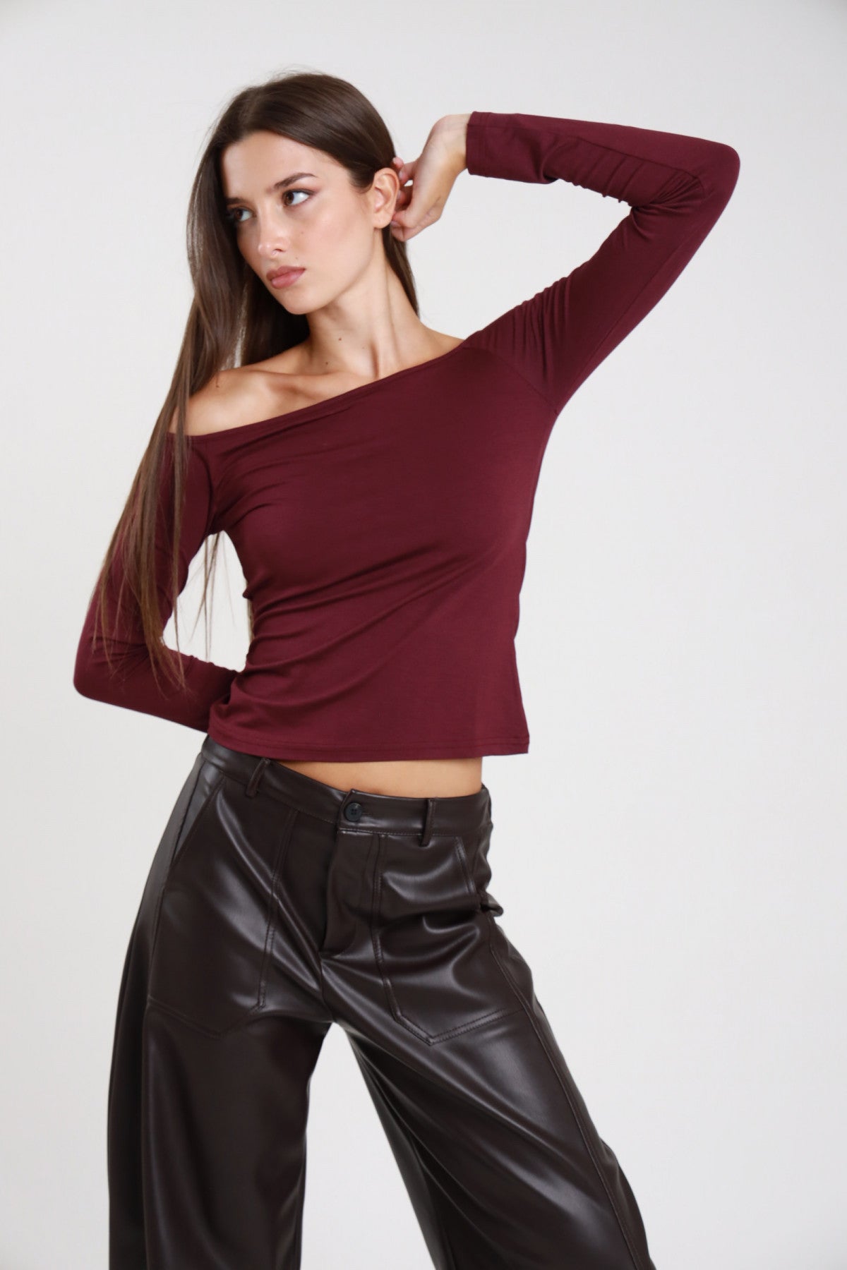 Maglia barchetta crop bordeaux donna con scollo a barchetta asimmetrico - vista laterale con pantaloni in ecopelle neri