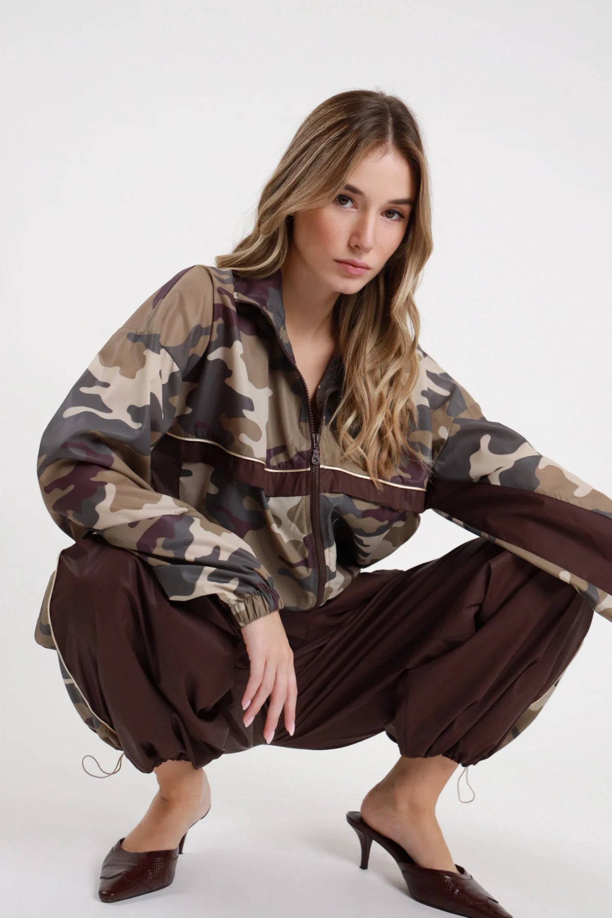 Bomber Camouflage Nylon 100% nylon camouflage zip aperta banda orizzontale cioccolato profilo beige visibile maniche balloon bordo cropped posa accovacciata total look coordinato - modella intera posa accovacciata sguardo frontale intenso capelli biondi sfondo bianco pantalone banda camouflage cioccolato total look coordinato mule tacco croco bordeaux