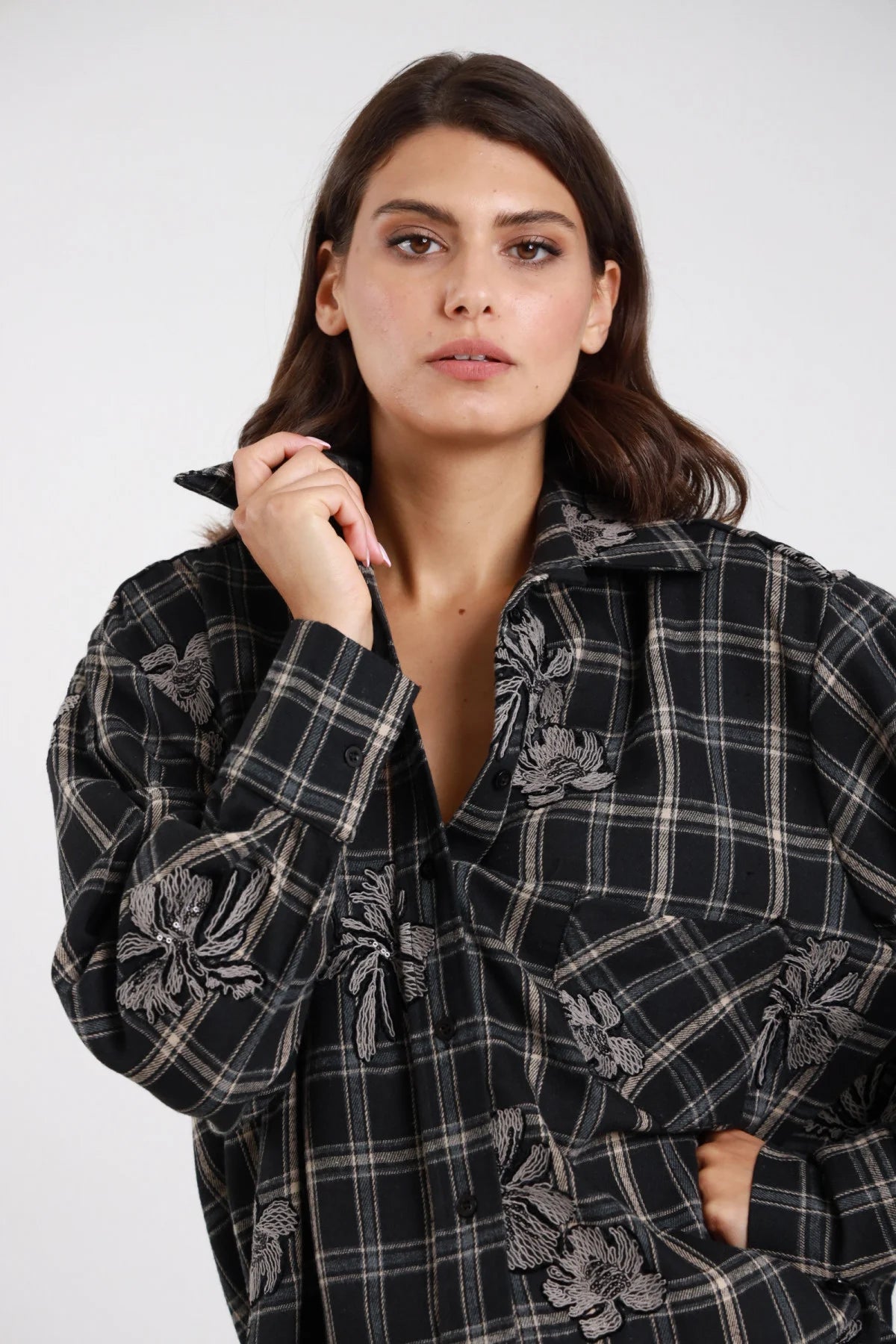 Camicia check ricamata tartan nero bianco grigio donna oversize colletto classico ricami floreali dettaglio - dettaglio frontale mezzo busto mano al colletto aperta con pantaloni neri