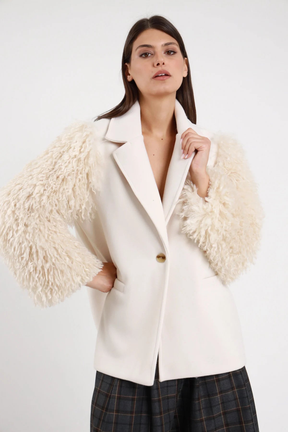 Blazer Maniche Ecopelliccia panna avorio 100% poliestere revers V sartoriale 1 bottone dorato tasche pattina maniche ecopelliccia panna riccioluta enormemente voluminose frontale busto mano revers - modella busto frontale mano revers sguardo frontale capelli castani lisci sfondo bianco pantalone tartan grigio abbinato