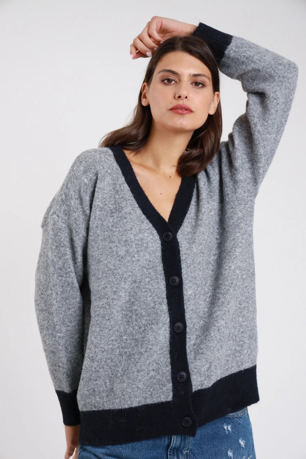 Cardigan bouclé teddy fluffy grigio melange mouliné bordatura profilo polsino fondo navy blu notte contrasto scollo V profondo abbottonatura frontale bottoni navy manica lunga ampia braccio alzato corpo oversize relaxed lunghezza vita hip fondo coste - modella frontale busto braccio sinistro alzato mano testa sguardo laterale basso capelli castani medi sfondo bianco jeans denim