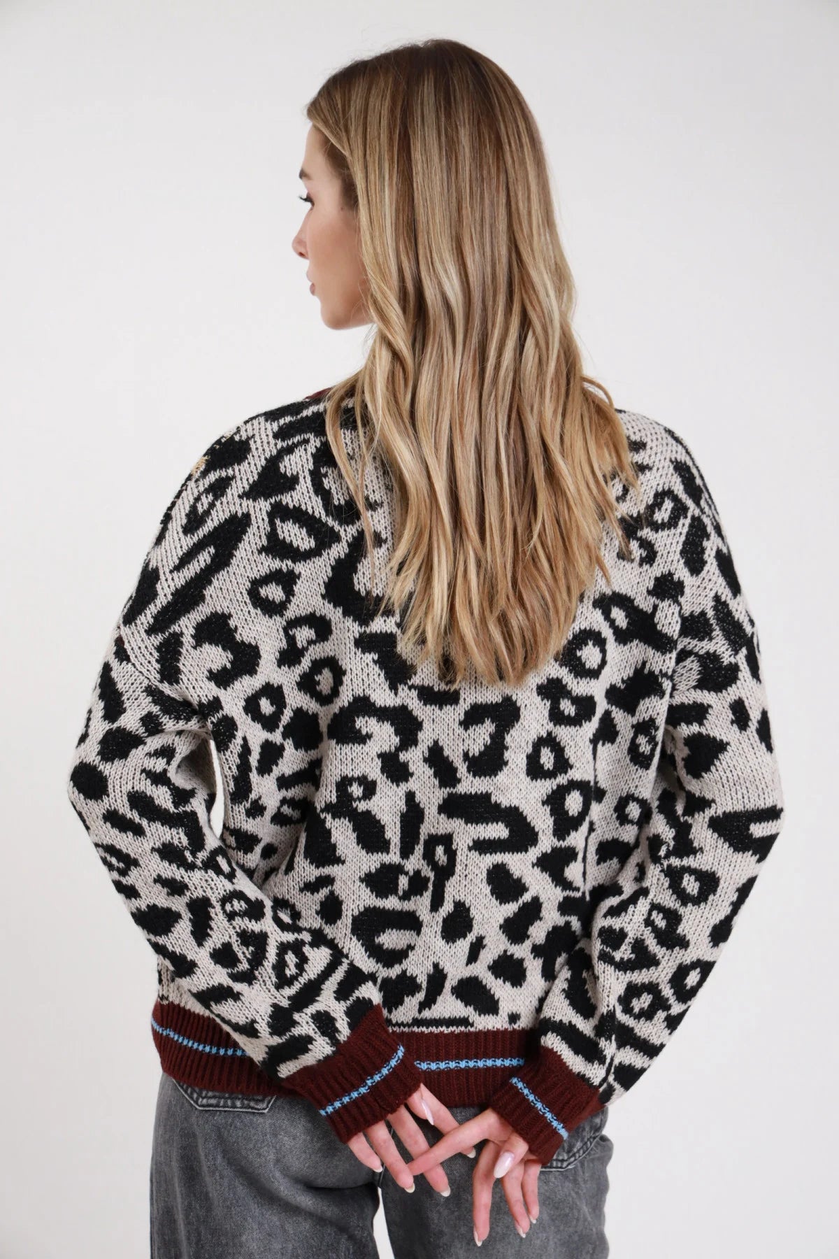 Cardigan animalier leopardato panna cammello oversize retro orlo costina bordeaux lurex azzurro - modella retro intera mani dietro schiena jeans grigi capelli biondi lunghi