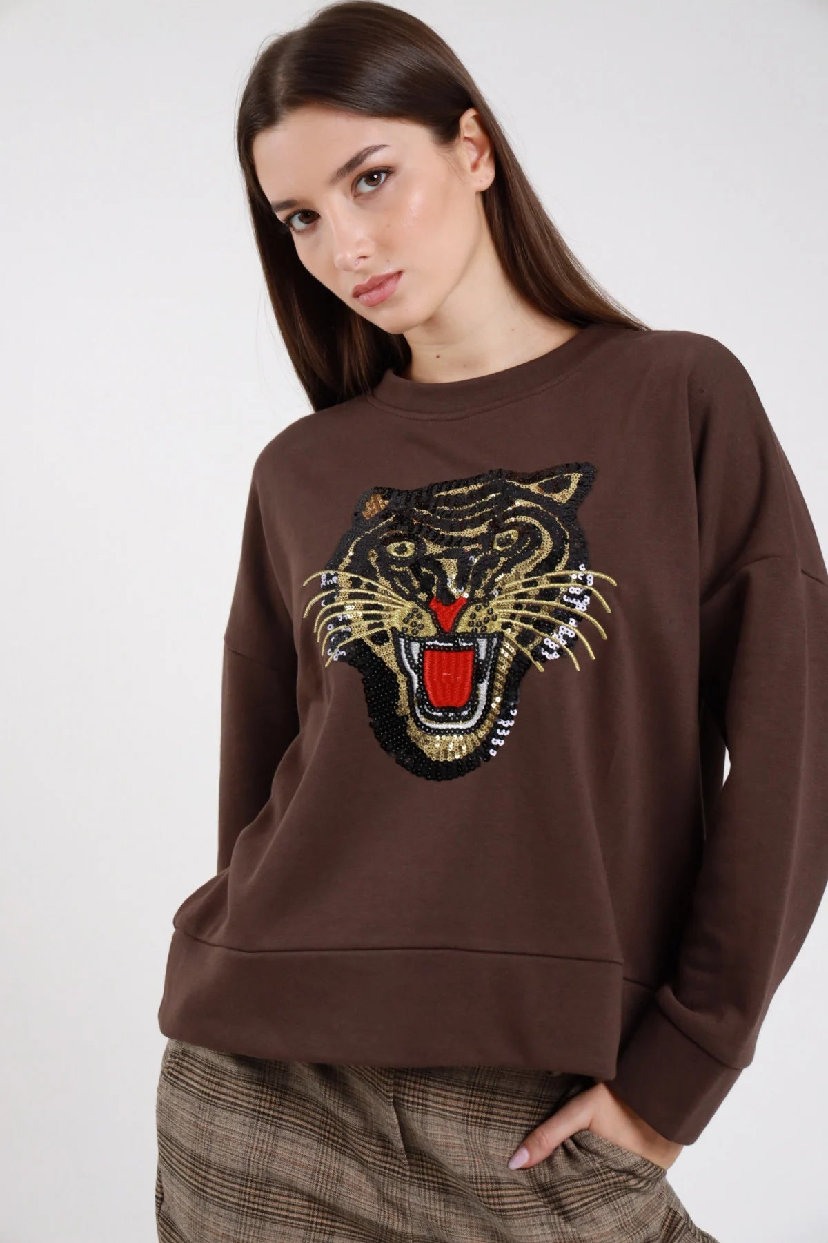 Felpa oversize cotone felpato marrone cioccolato maxi patch ricamo paillettes tigre ruggente oro nero rosso girocollo tondo frontale busto tigre medio mano collo - modella frontale busto mano collo sguardo frontale capelli castani scuri lisci lunghi sfondo bianco pantaloni check beige