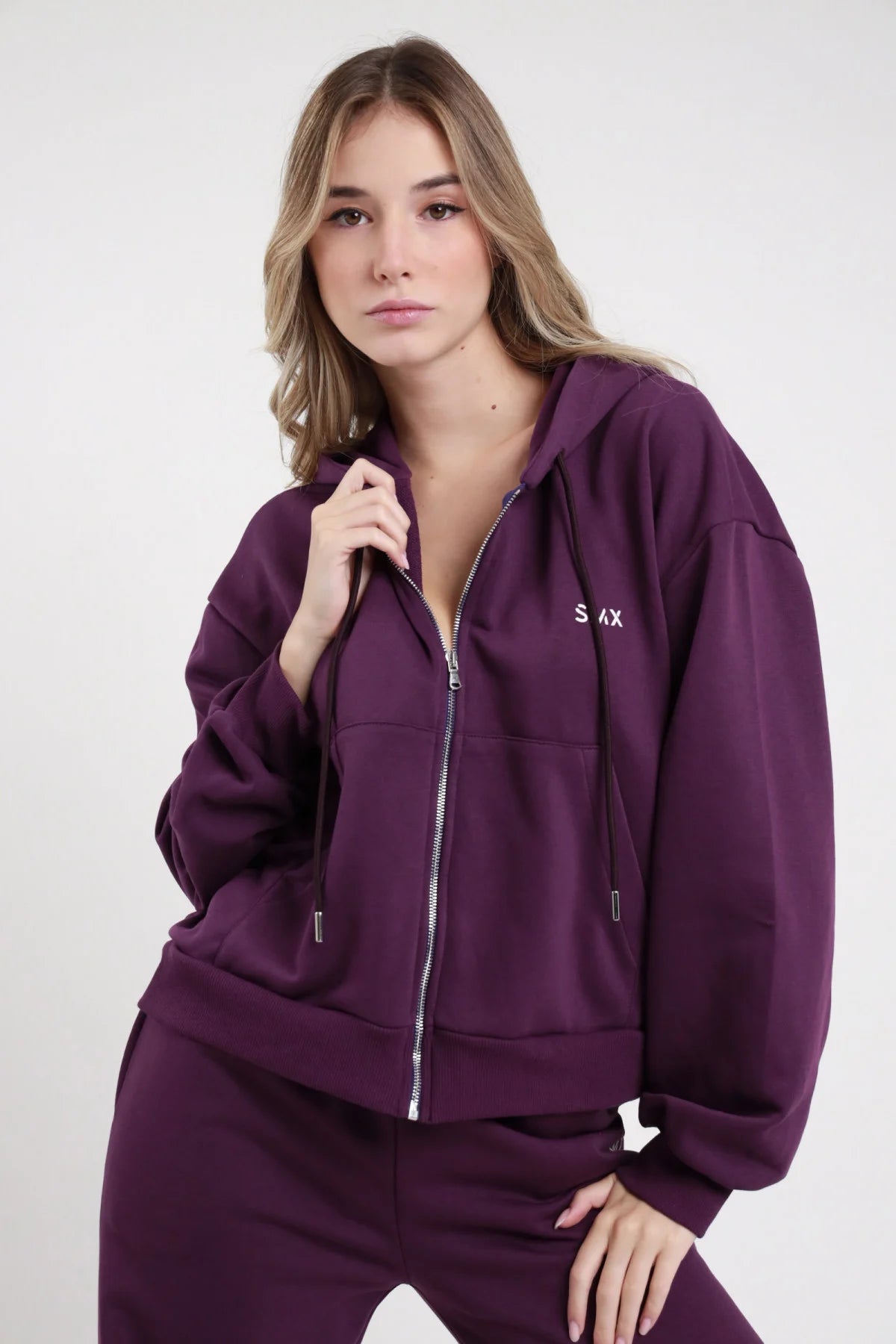 Felpa Zip SMX Limited Edition viola melanzana logo SMX petto sinistro zip frontale aperta cappuccio coulisse tasche fianchi zip laterali manica oversize balloon busto 3/4 mano zip sguardo frontale - modella busto 3/4 mano zip sguardo frontale capelli castani mossi sfondo bianco pantalone wide leg viola coordinato abbinato