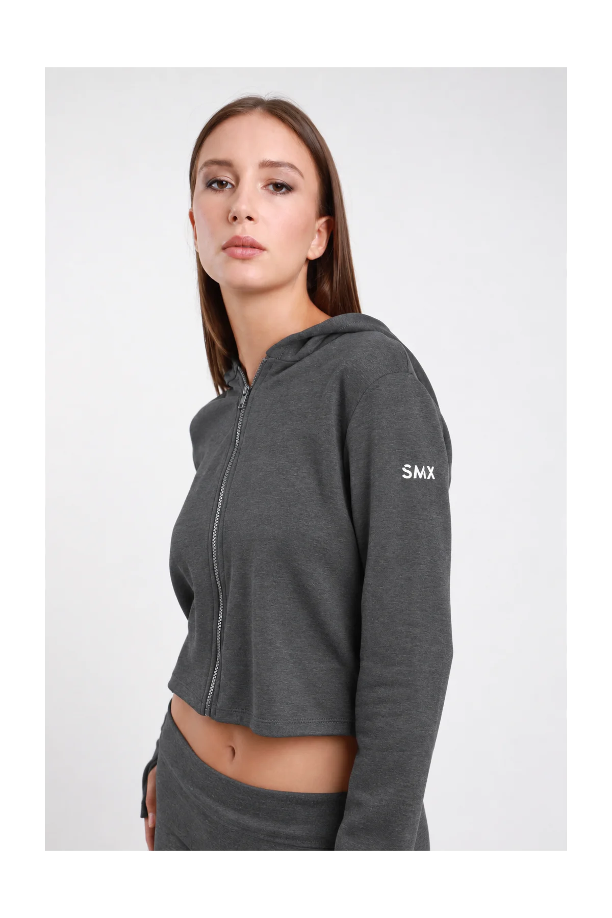 Felpa Crop Zip DAYTHRU grigio antracite melange cappuccio zip frontale logo SMX bianco manica ben visibile orlo crop polsino foro pollice crop fit busto laterale 3/4 sguardo frontale - modella busto laterale 3/4 sguardo frontale capelli castani lisci sfondo bianco coordinato grigio antracite pantalone wide-leg