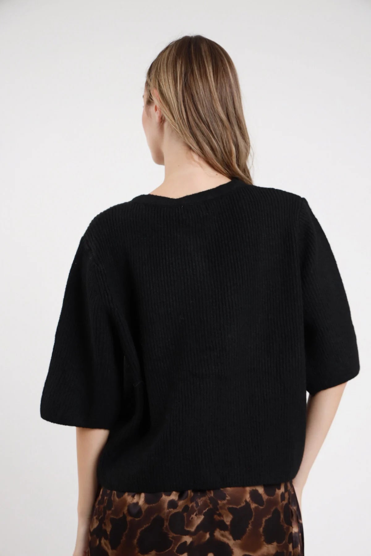 Cardigan Maniche Corte nero maglia costine manica corta boxy oversize spacco laterale retro liscio posteriore busto - modella busto posteriore capelli biondi lisci sfondo bianco gonna leopardata animalier minigonna frange abbinata coordinata