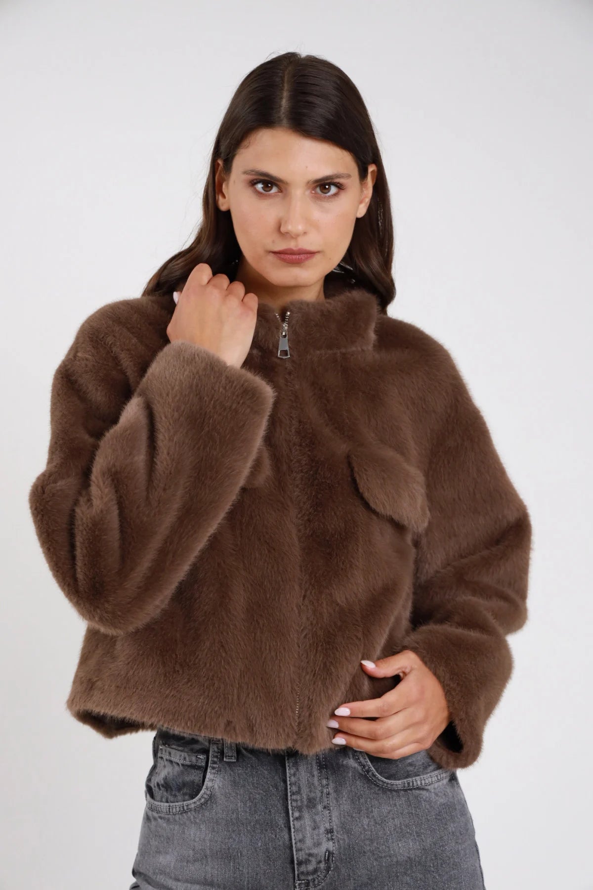 Ecopelliccia teddy bomber zip colletto alto taschino polsino cuff oversize boxy crop marrone medio tabacco frontale busto mano zip colletto taschino visibile - modella frontale busto mano zip colletto taschino visibile sguardo frontale capelli castani scuri lisci sfondo bianco jeans grigio