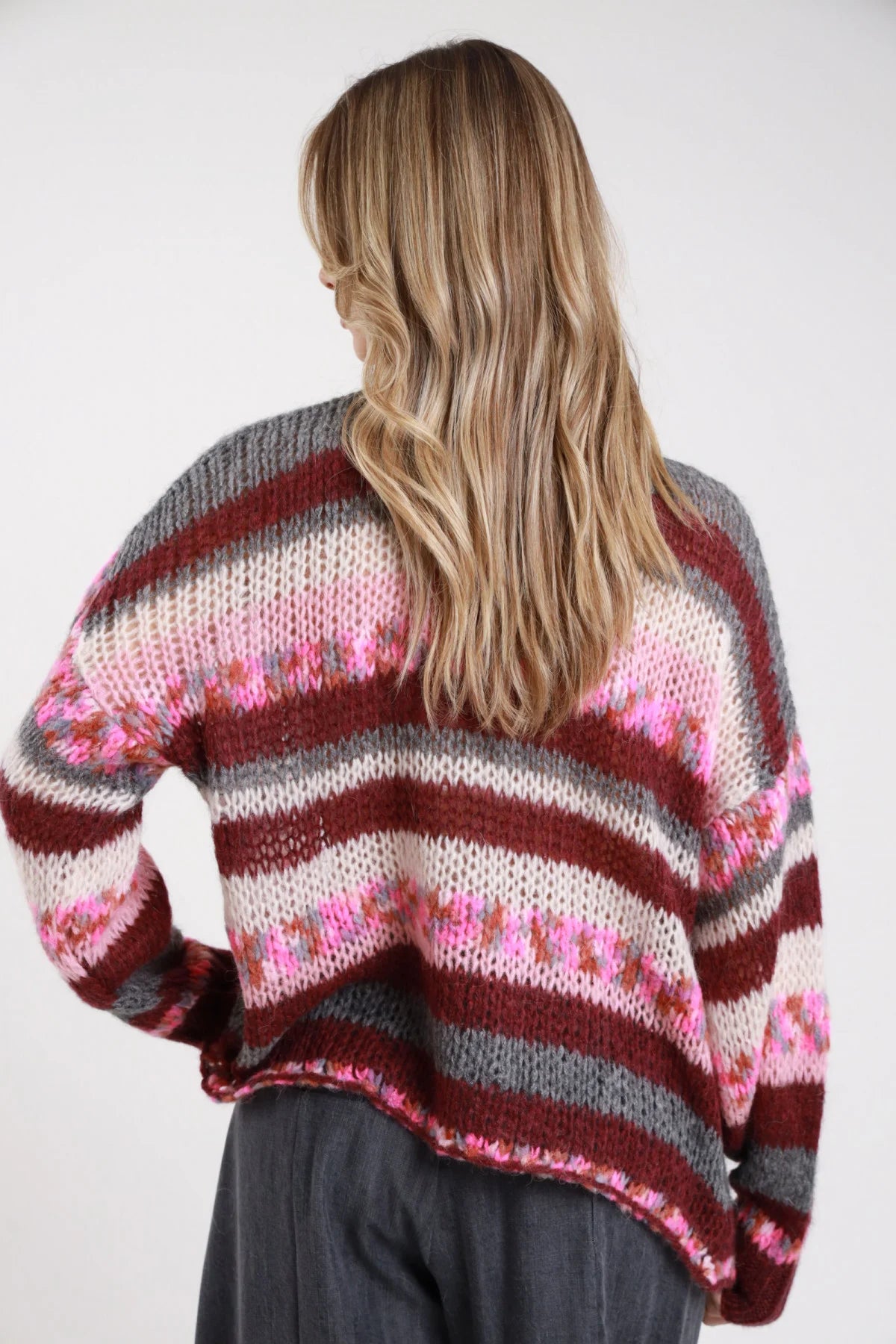 Cardigan righe multicolor grigio bordeaux rosa panna maxi oversize - modella retro intera mani sui fianchi sguardo laterale jeans grigi capelli biondi mossi