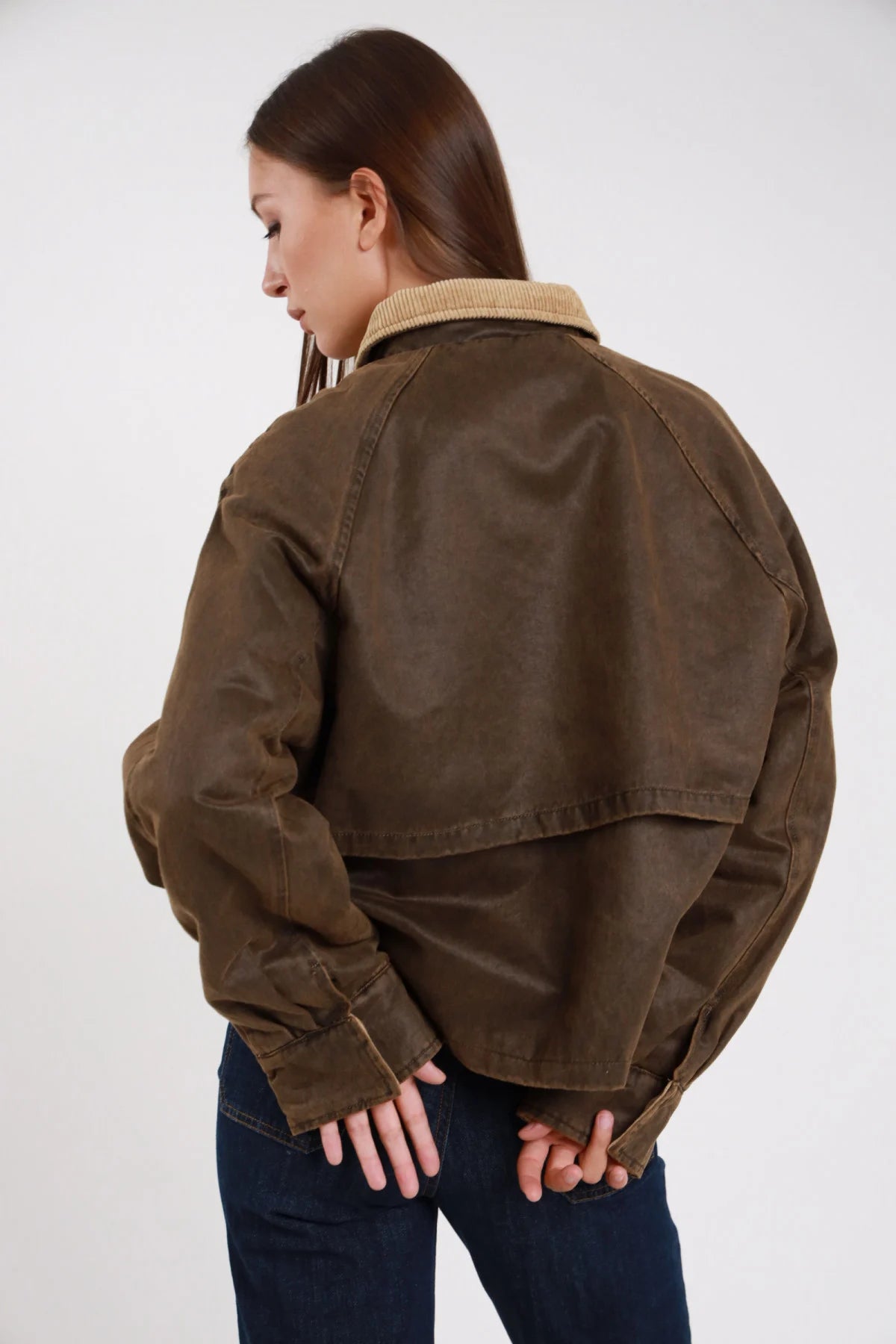 Giacca ecopelle cerata waxed verde khaki retro tre quarti yoke raglan cuciture contrasto corpo oversize boxy - modella retro tre quarti mani incrociate dietro sguardo basso laterale jeans indaco capelli castani lisci