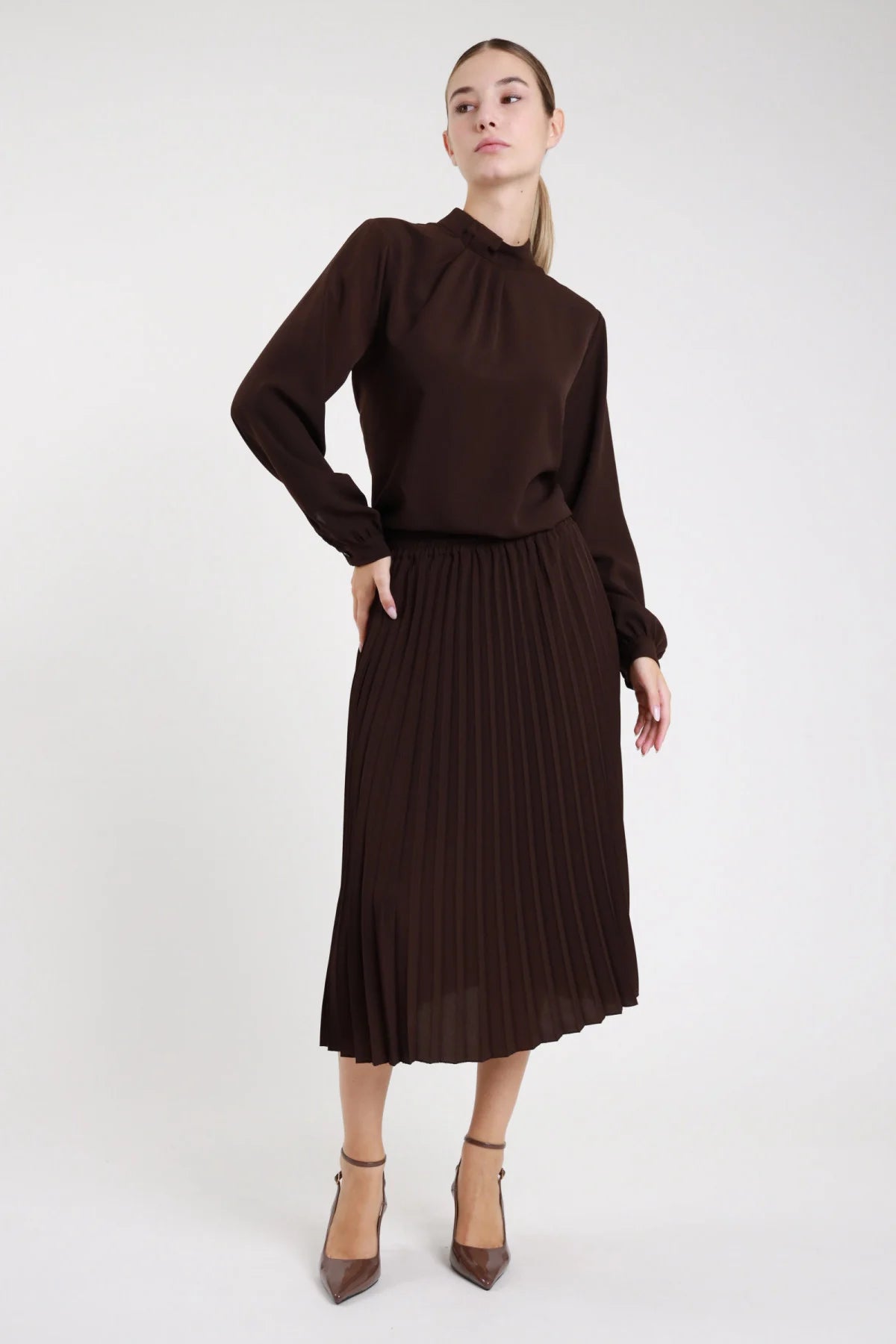 Gonna plissettata midi cioccolato scuro tessuto fluido - modella frontale intera tre quarti mano in tasca con blusa abbinata e décolleté grigi capelli castani lisci
