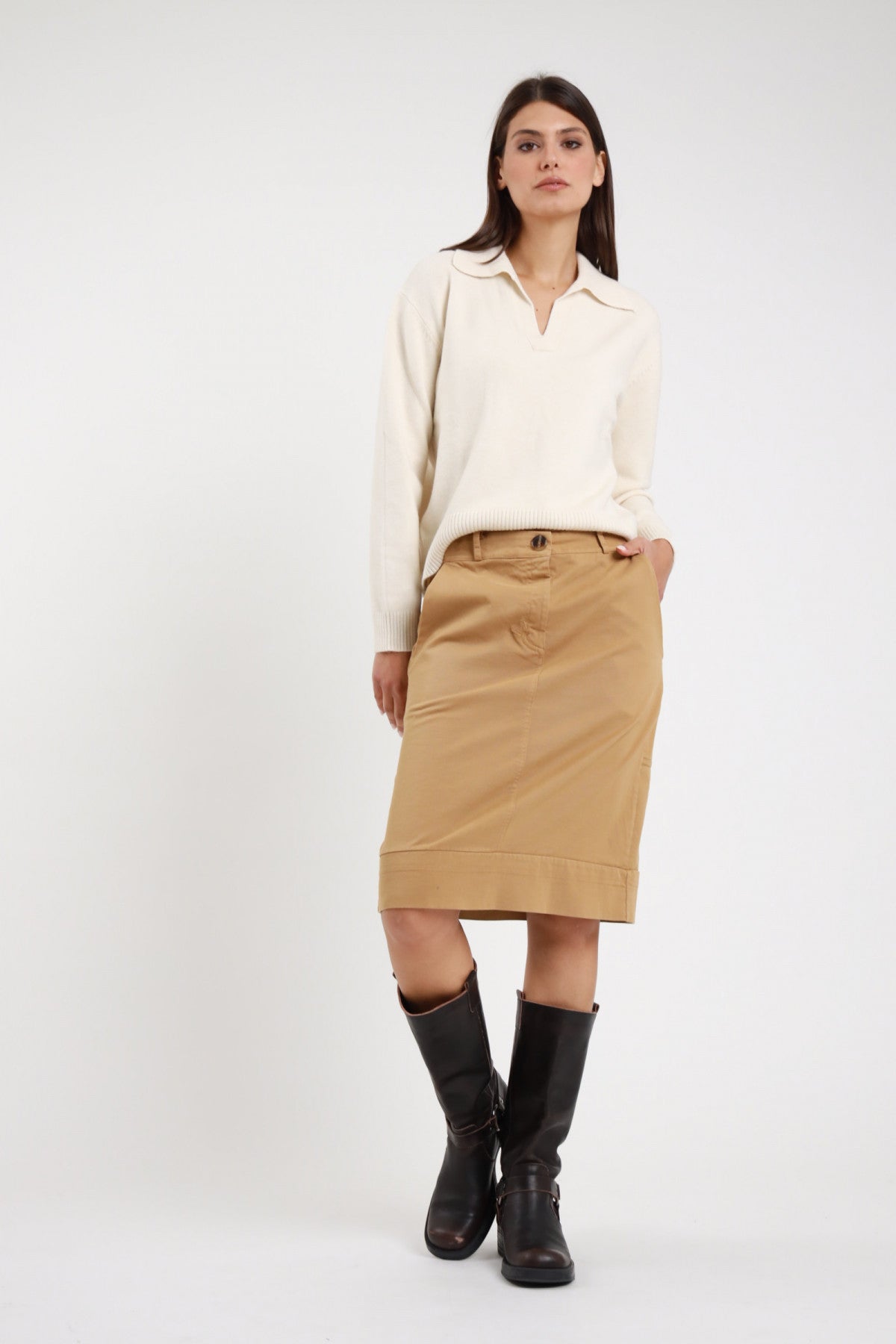 Gonna tasche midi Susy Mix Pre-Fall beige cammello vita alta bottone grande scuro passanti cintura tasche laterali risvolto turn-up fondo mano tasca frontale busto intera - modella frontale intera mano tasca capelli scuri lisci sfondo bianco maglione polo panna stivali biker neri abbinati