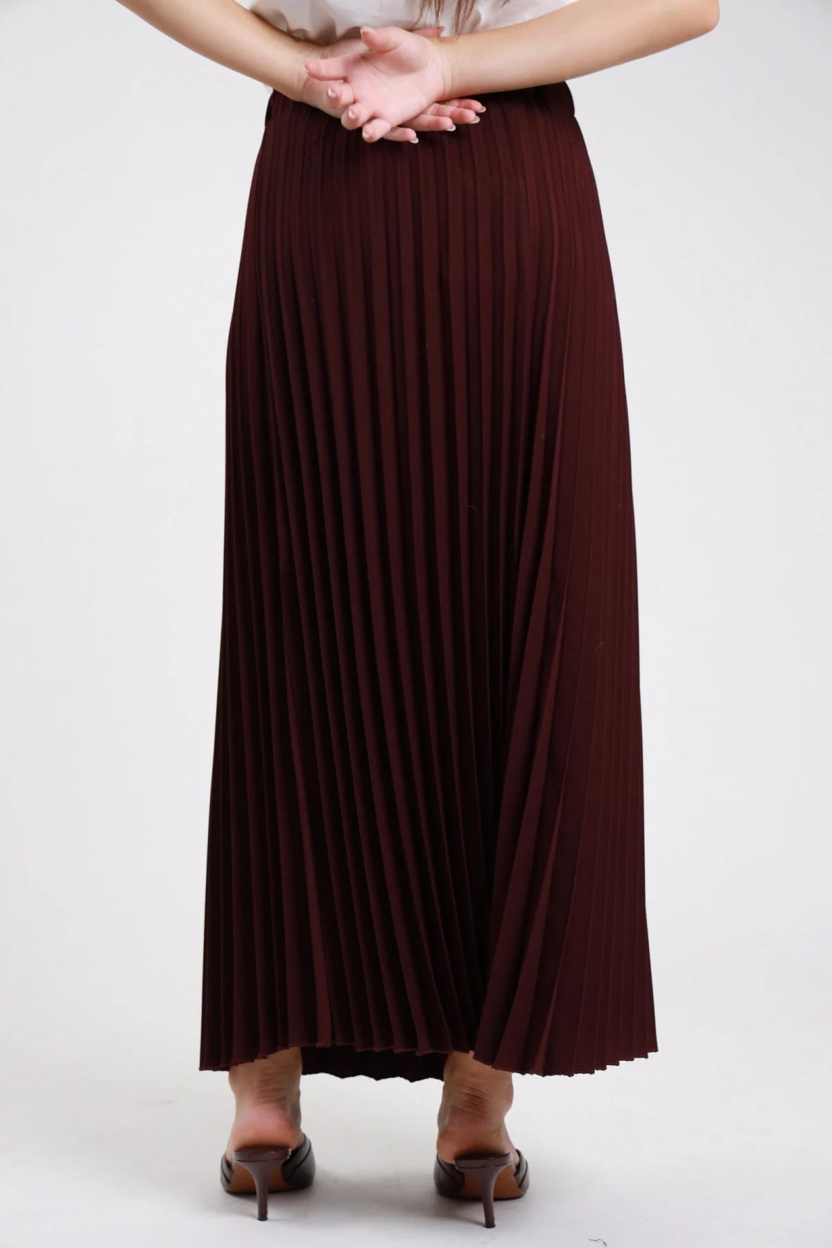 Gonna lunga plissé bordeaux prugna vinaccia retro busto dettaglio vita alta elastico invisibile plissé fitto permanente allover caduta fluente svasata mani giunte - modella retro busto mani giunte sguardo frontale sandali tacco mules marroni sfondo bianco