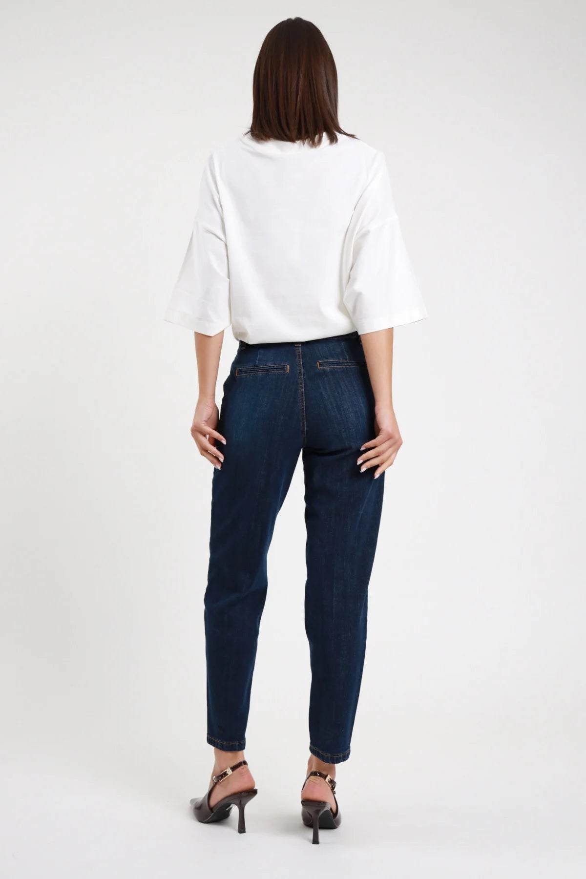 Jeans Chino Slim Vita Alta blu scuro indaco 98% cotone tasche posteriori piatte stile chino senza toppa gamba dritta affusolata fondo cropped pulito posteriore intera - modella intera posteriore posa statica capelli castani lisci sfondo bianco t-shirt bianca oversize slingback marrone tacco