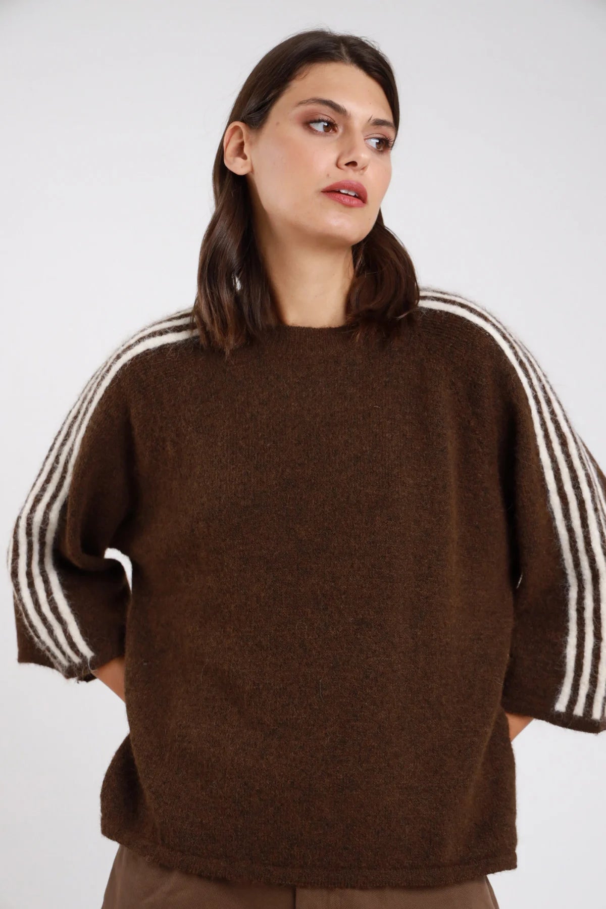 Pullover bande strisce contrasto manica cioccolato moro marrone scuro corpo bande bianche panna verticali 3-4 righe alternate batwing dolman manica 3/4 girocollo oversize boxy vita orlo dritto maglia bouclé alpaca-like - modella frontale busto tre quarti sguardo laterale alto capelli castani mosci sfondo bianco pantaloni marroni bermuda