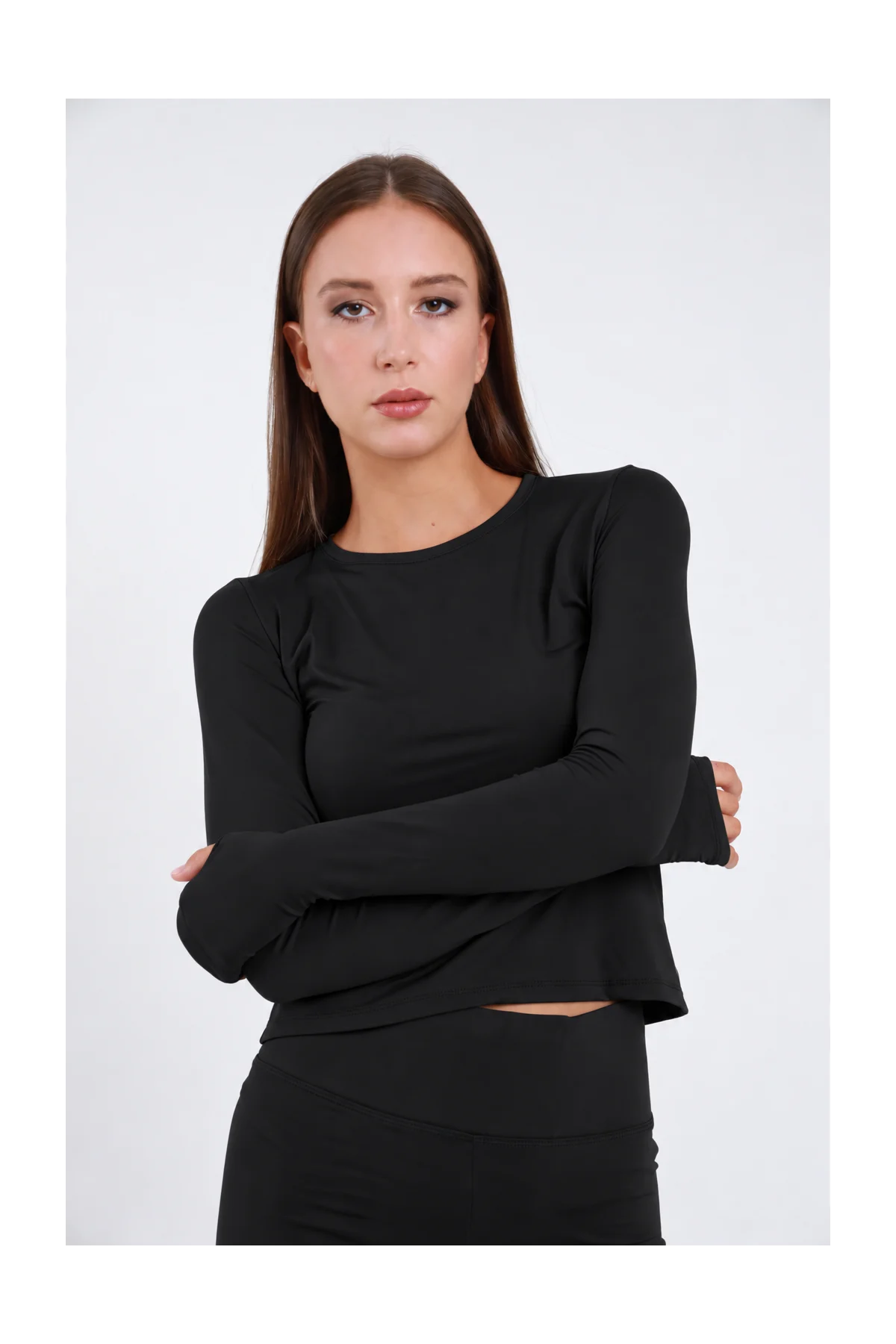 Maglia Second-Skin DAYTHRU nero manica lunga aderente collo tondo polsino foro pollice silhouette body-con busto frontale 3/4 braccia conserte sguardo frontale - modella busto frontale 3/4 braccia conserte sguardo frontale capelli castani lisci sfondo bianco coordinato nero gonna pantalone