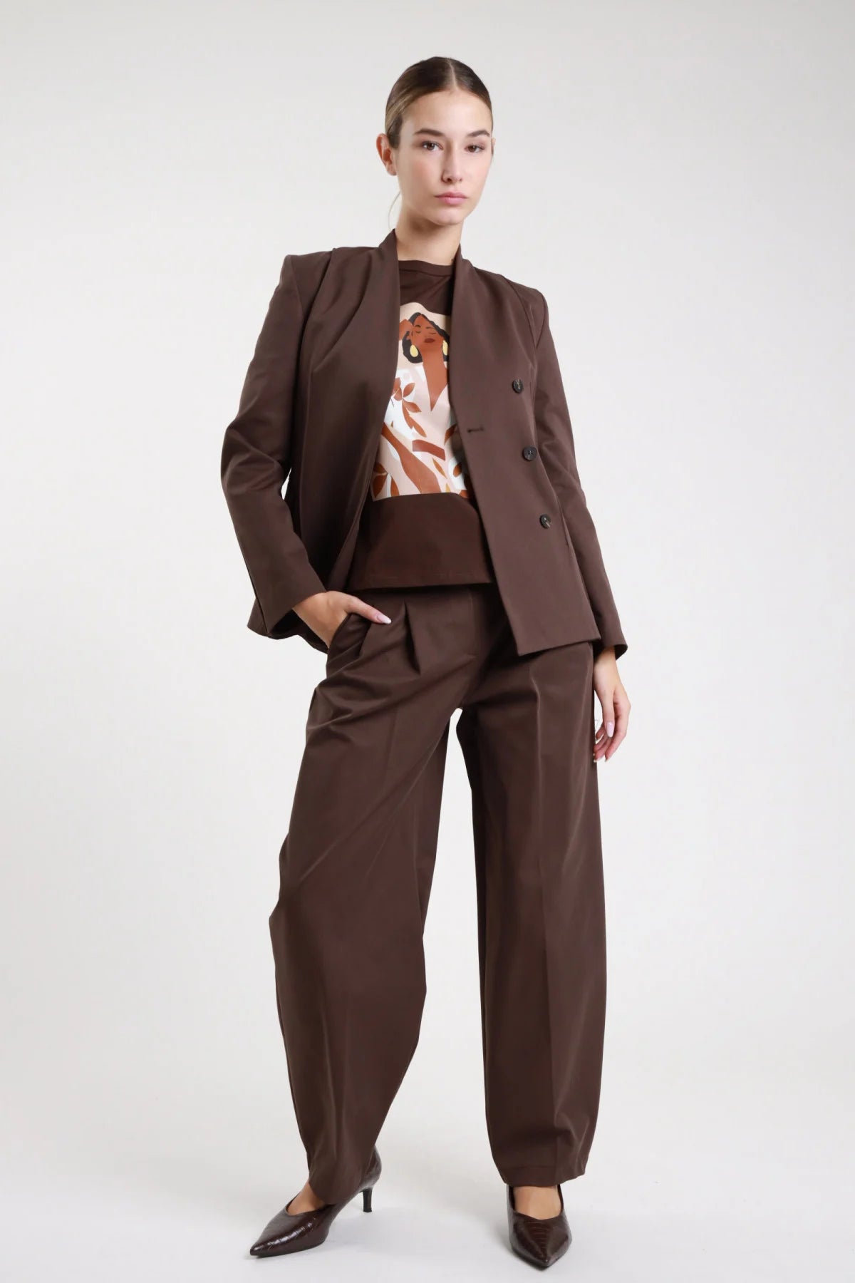 Pantaloni doppia pinces cioccolato scuro dritti sartoriali - modella frontale intera con blazer doppio petto e t-shirt illustrazione décolleté marroni capelli raccolti