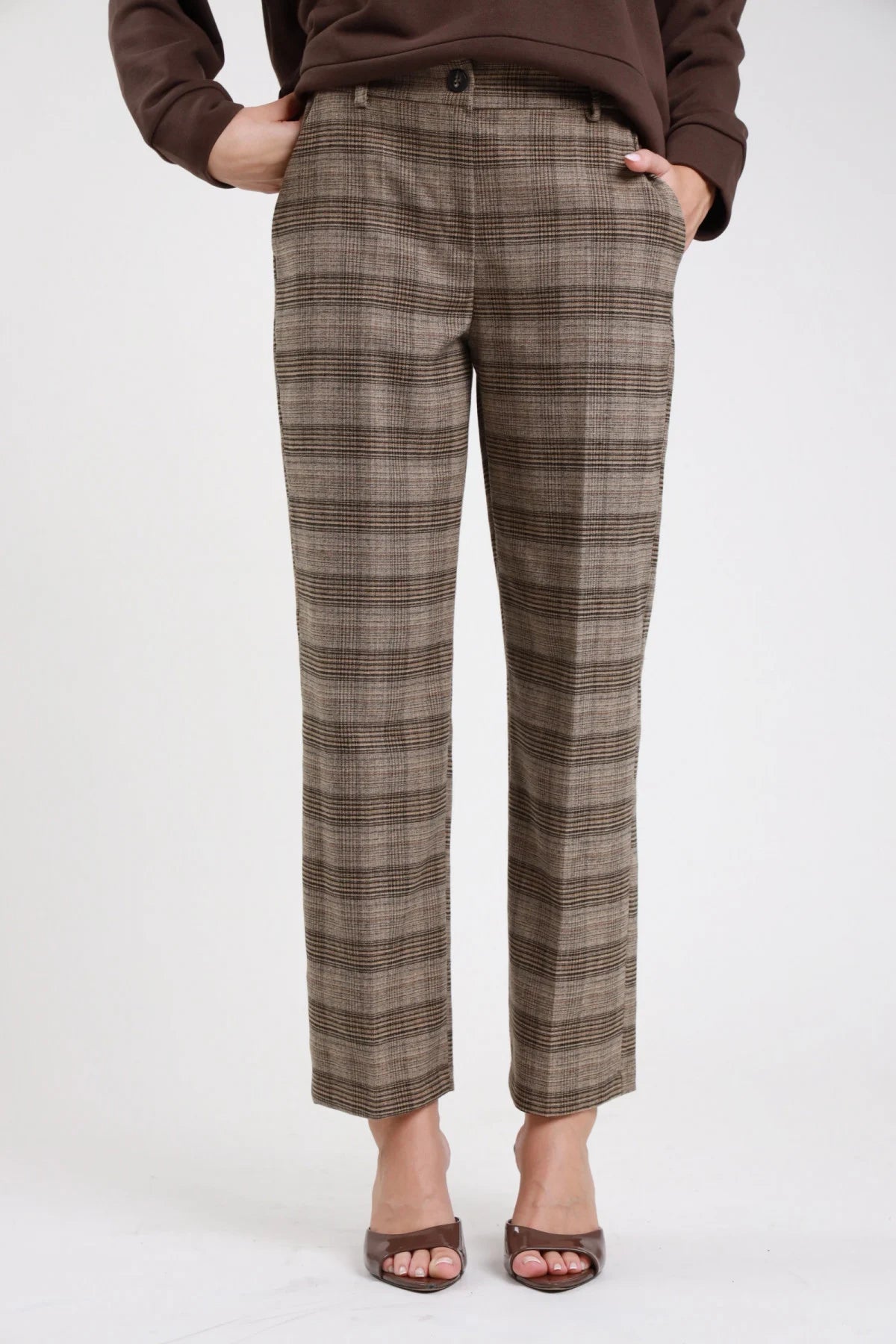 Pantaloni check principe di Galles sartoriali beige marrone nero gamba dritta straight piega centrale caviglia seduta pavimento braccio alzato testa - modella seduta pavimento braccio alzato testa sguardo frontale capelli castani lisci lunghi sfondo bianco mules tacco marroni felpa marrone tigre paillettes