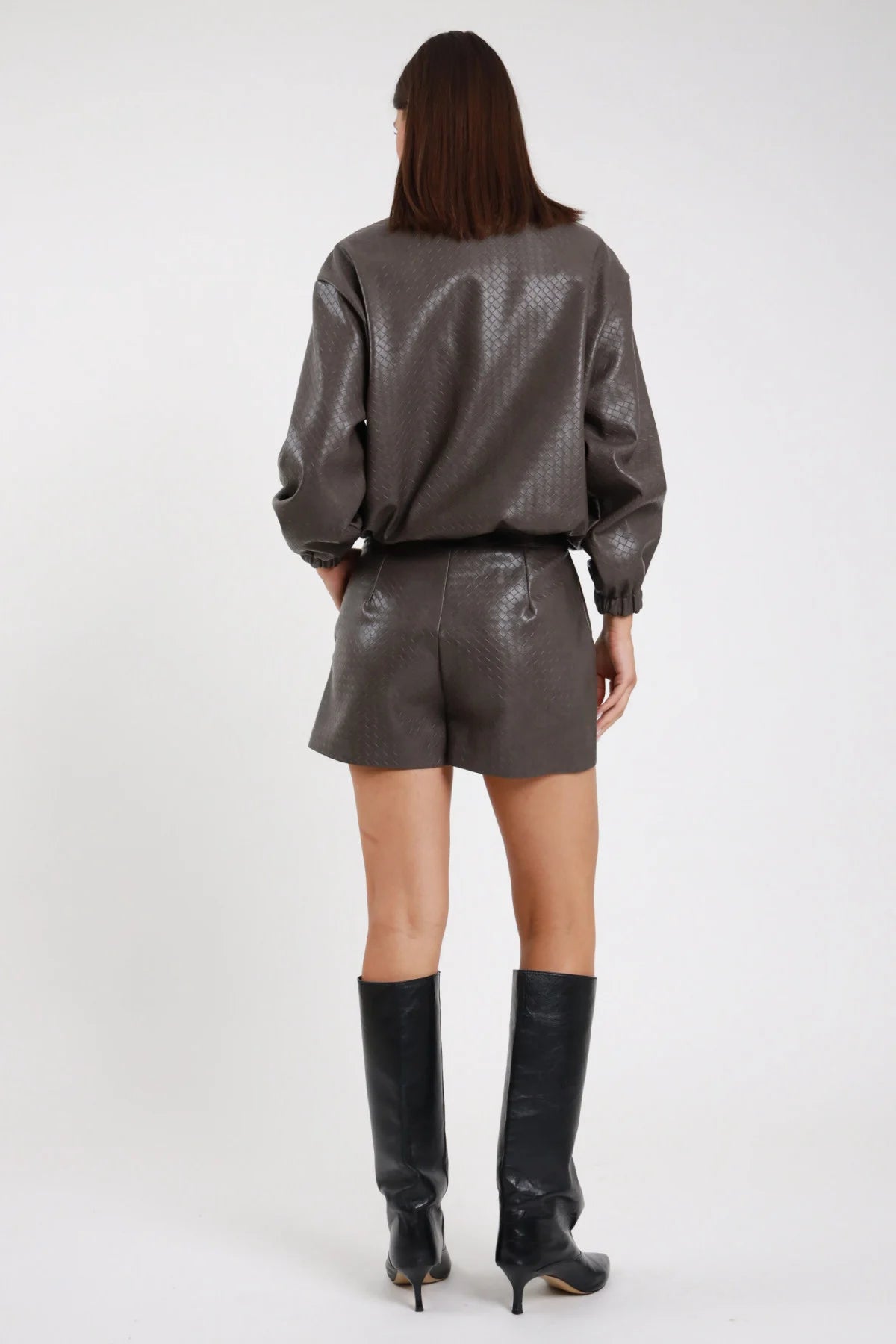Short Ecopelle Intrecciato grigio talpa antracite woven embossed romboidale mini wide leg vita alta elastica retro intera coordinato bomber intrecciato grigio - modella retro intera sguardo abbasso capelli castani sfondo bianco bomber intrecciato grigio coordinato stivali neri tacco