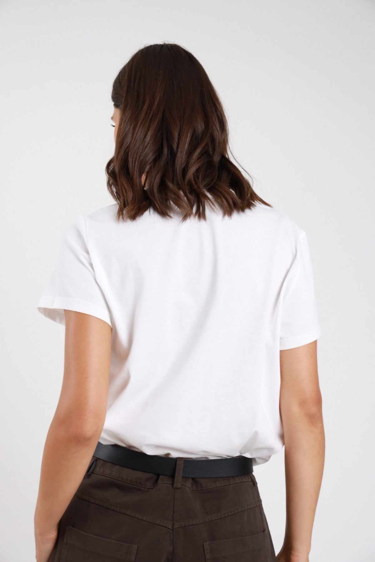 T-shirt bianca retro intera jersey cotone girocollo manica corta regular relaxed lunghezza vita orlo dritto - modella retro intera capelli castani mossi pantaloni marroni scuri cintura nera sfondo bianco grigio