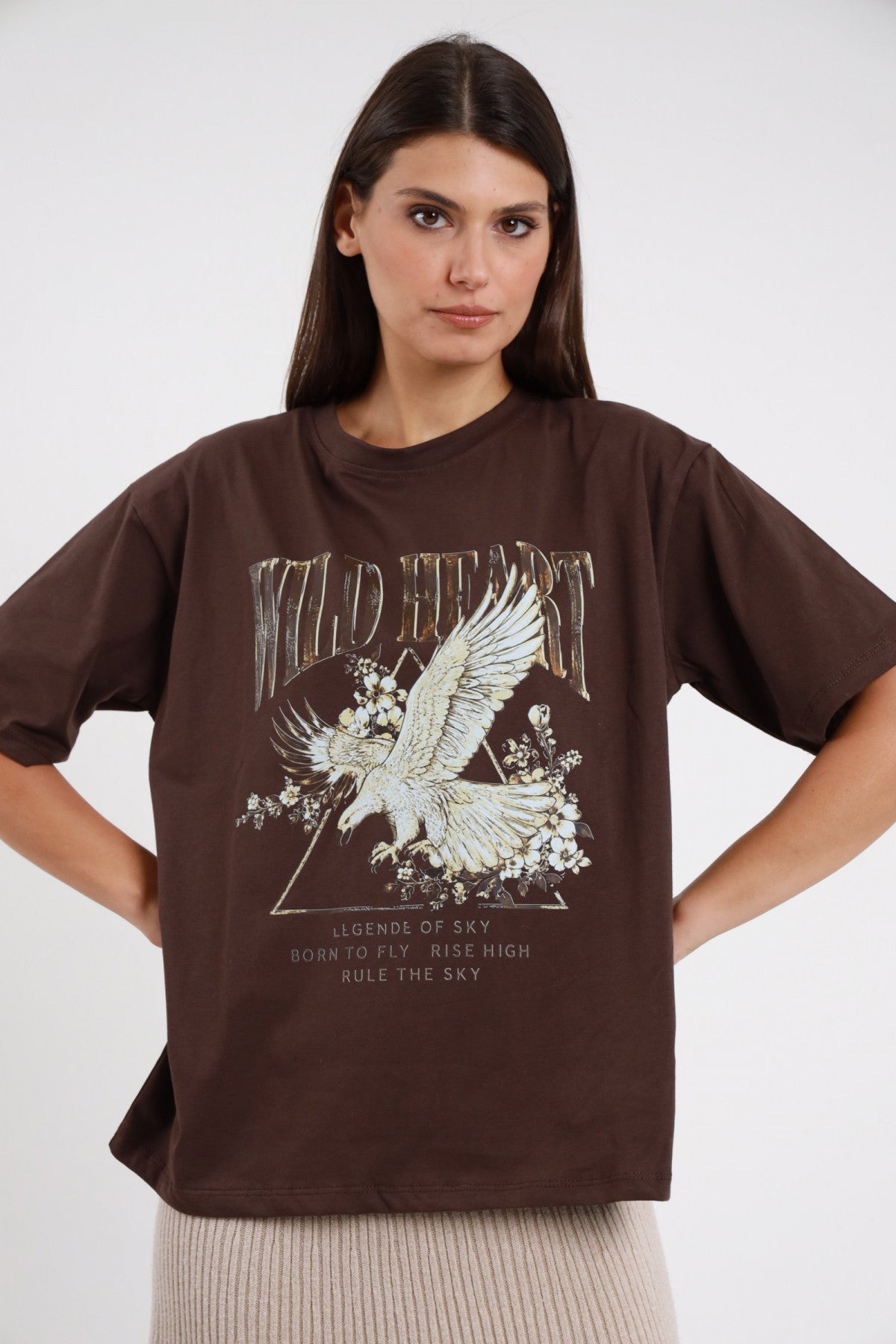T-shirt Wild Heart Susy Mix Pre-Fall marrone tabacco cioccolato 100% cotone stampa frontale Wild Heart aquila dorata fiori Born to Fly Rule the Sky girocollo manica corta oversize relaxed busto frontale mani fianchi sguardo frontale - modella busto frontale mani fianchi capelli scuri lisci sfondo bianco gonna coste beige avena abbinata