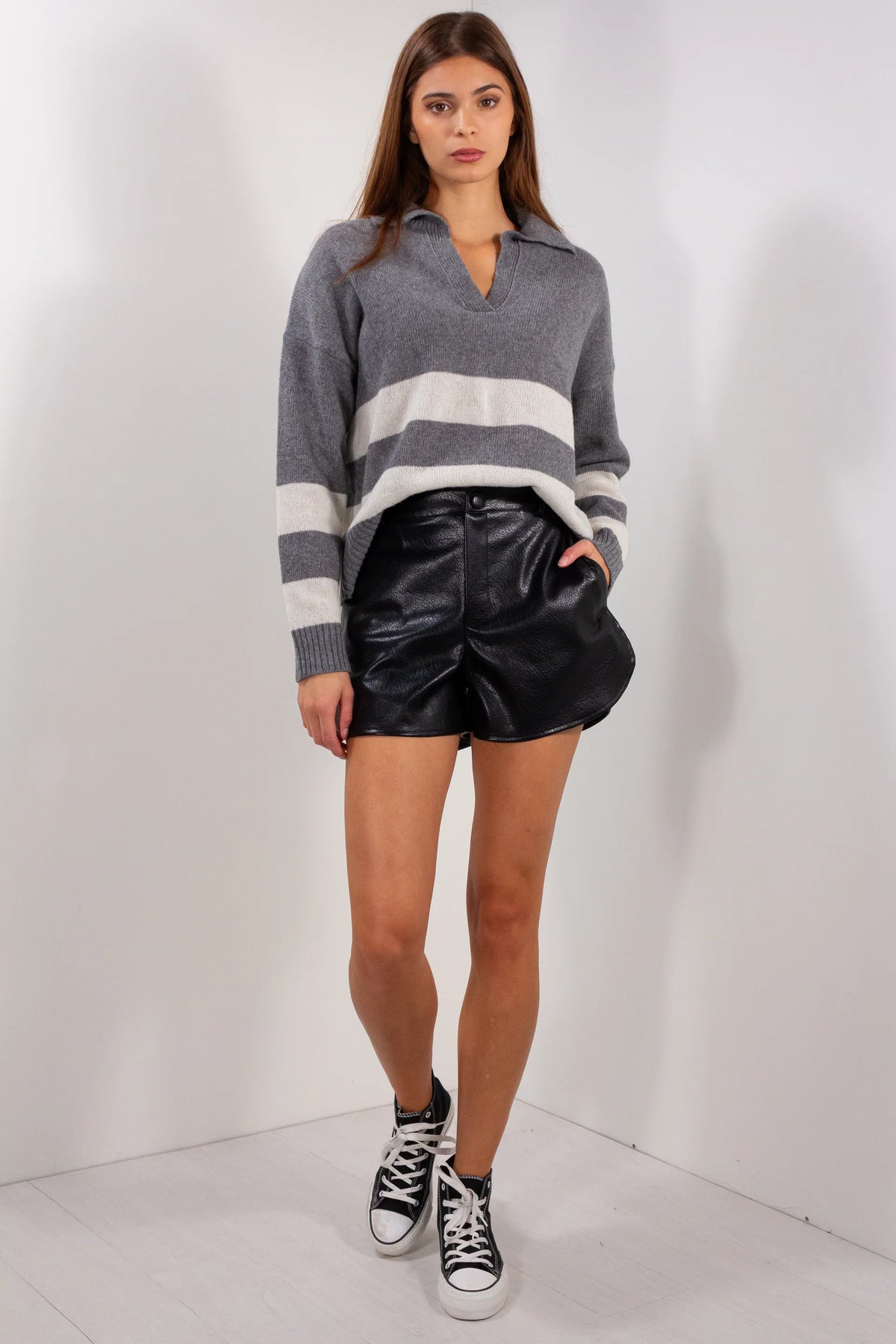 Shorts ecopelle Duda neri indossati con maglia grigia a righe e sneakers, vista frontale