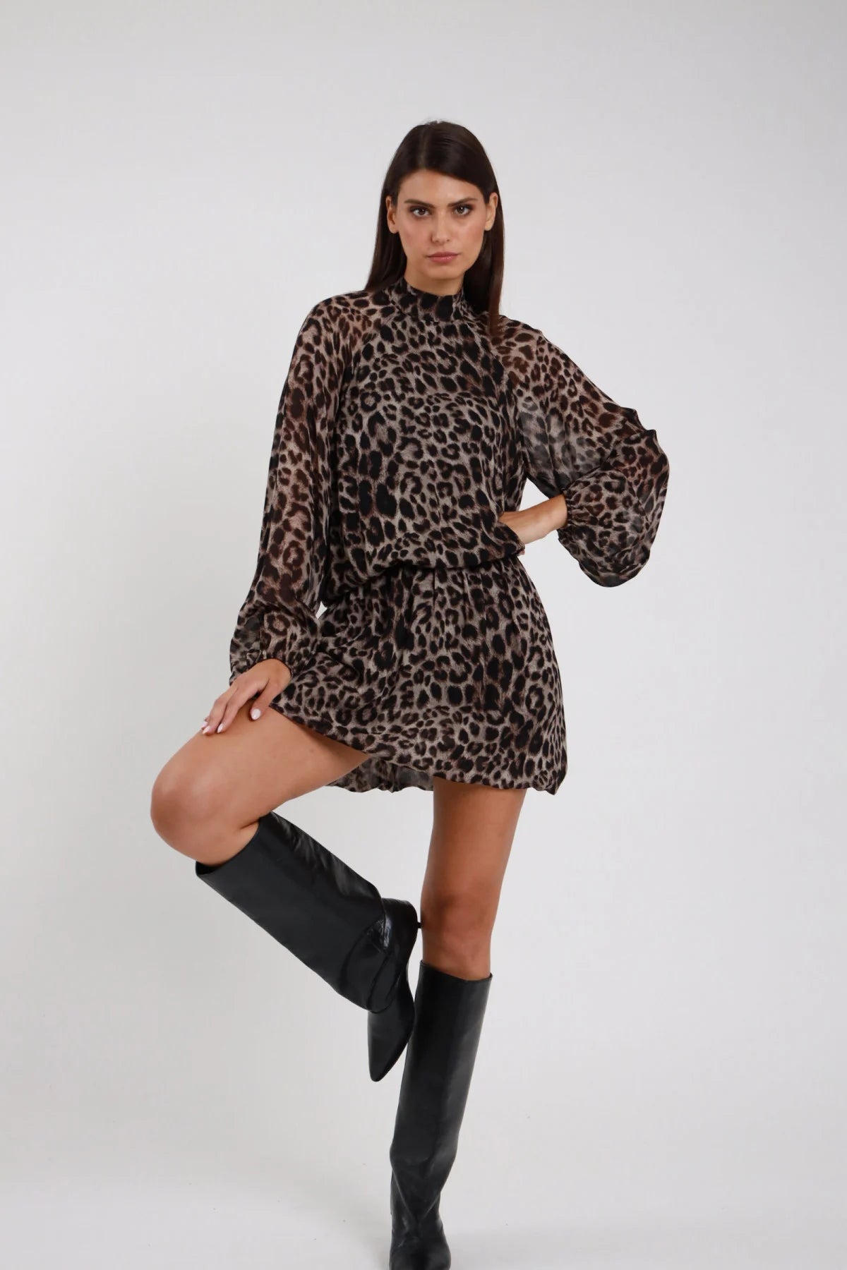 Abito Animalier leopardato maculato beige marrone nero viscosa colletto alto rouches manica batwing cintura elastica gonna mini arricciata frontale intera gamba alzata posa dinamica - modella frontale intera gamba alzata sguardo frontale capelli castani lisci sfondo bianco stivali neri alti ginocchio