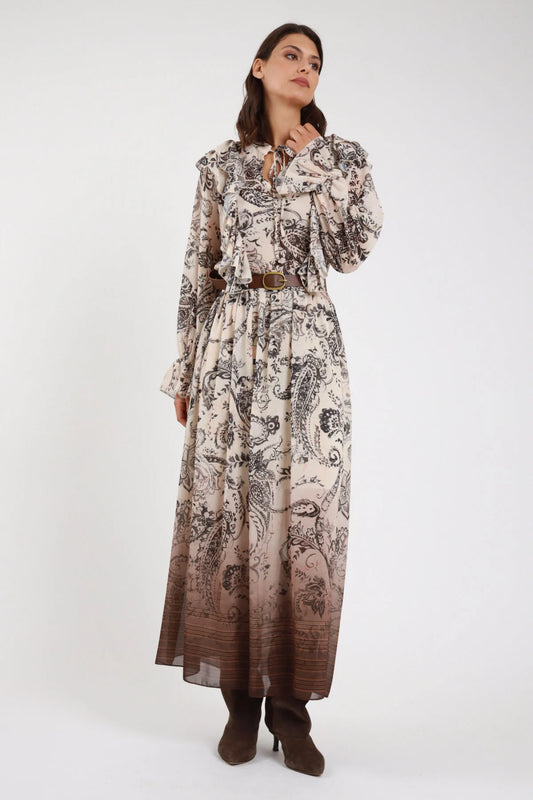 Abito lungo fantasia paisley baroque chiffon panna ecru cioccolato moro degrade frontale busto mano collo fiocco lavalliere colletto fiocco volant ruches spalle abbottonatura frontale nascosta cintura ecopelle marrone fibbia gold manica lunga polsino balze - modella frontale busto mano collo fiocco sguardo laterale alto stivali marroni capelli castani mossi sfondo bianco