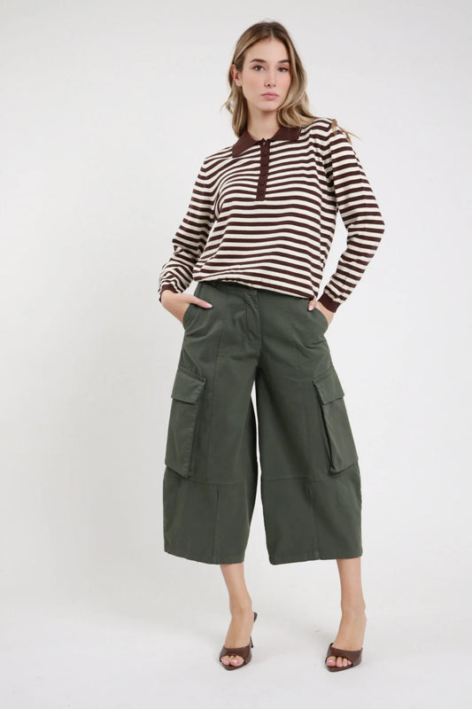 Bermuda Tasconi verde militare oliva 97% cotone vita alta zip bottone tasche laterali oblique 2 grandi tasconi cargo applicati pattina bottone gamba wide leg culotte lunghezza polpaccio frontale intera mani tasche - modella intera frontale mani tasche sguardo frontale capelli biondi ondulati sfondo bianco polo maglia righe cioccolato panna mule tacco cioccolato