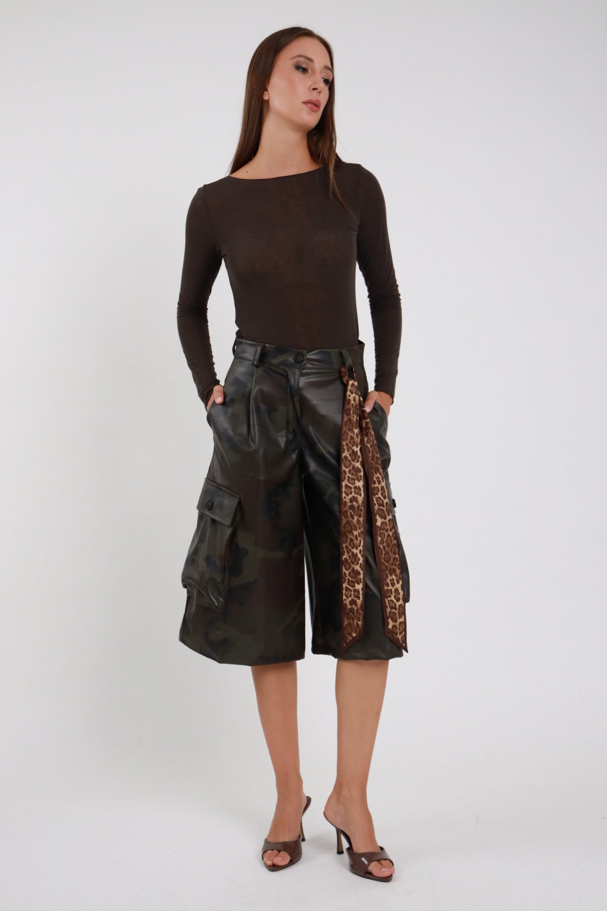 Bermuda Mimetico cargo culottes ecopelle PU camouflage verde bronzo tasconi laterali patta cintura leopardata vita alta frontale intera mani tasche - modella frontale intera mani tasche sguardo frontale capelli castani lisci sfondo bianco top marrone mules tacco marrone