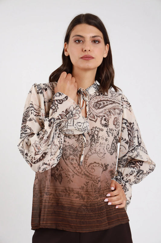 Blusa fantasia paisley baroque chiffon panna ecru cioccolato moro degrade frontale busto mano collo scollo V profondo laccetto fiocco drappeggiante manica balloon bishop polsino balze ruches svasato degrade cioccolato bordura tessuta fondo - modella frontale busto mano collo fiocco sguardo frontale intenso pantaloni marroni capelli castani mossi sfondo bianco