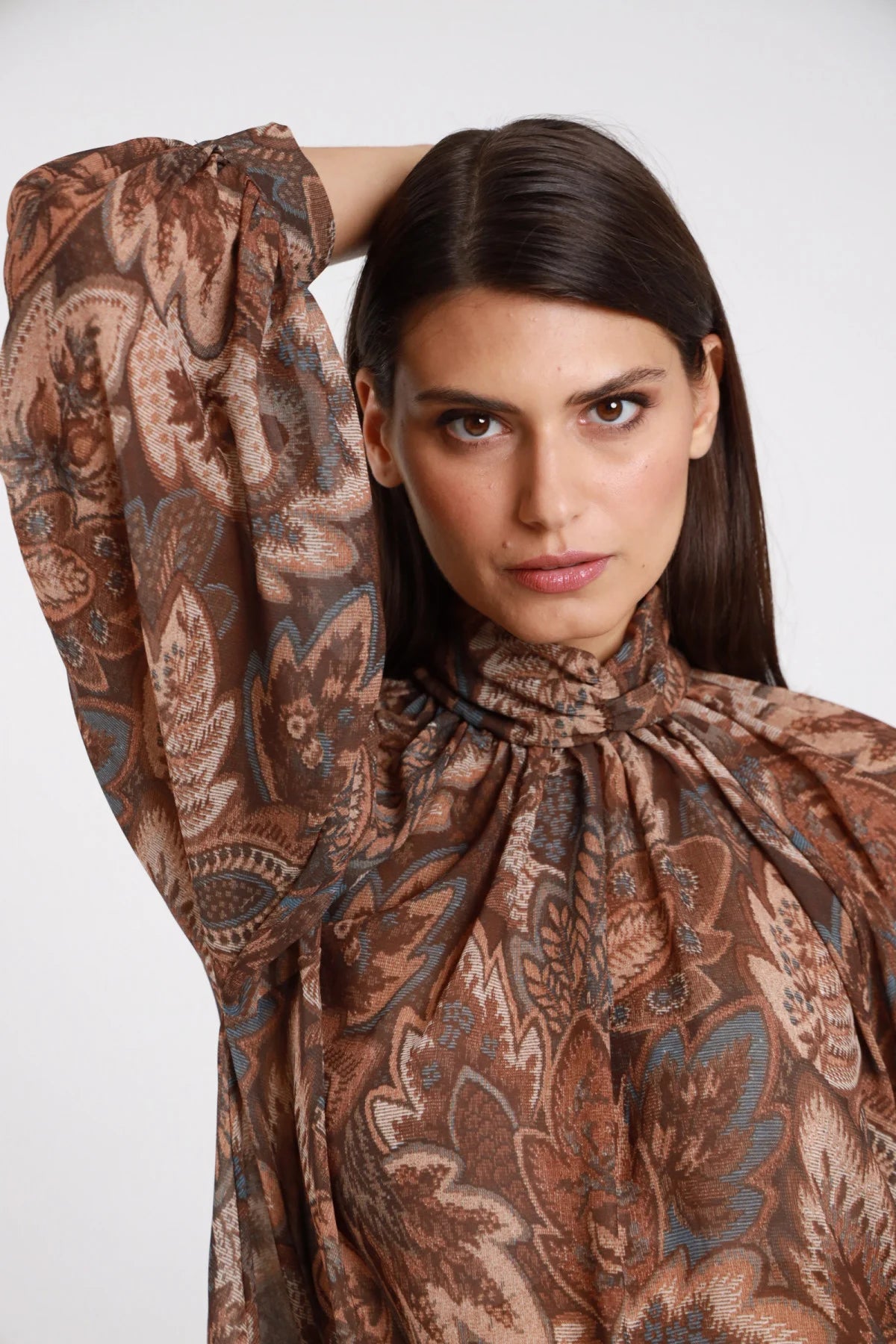 Blusa Lupetto Fantasia Paisley Cachemire chiffon marrone tabacco colletto lupetto arricciato coulisse polsino elastico manica balloon close-up dettaglio busto frontale 3/4 braccio alto - modella busto frontale 3/4 braccio alto sguardo intenso capelli castani lisci sfondo bianco stampa paisley primo piano