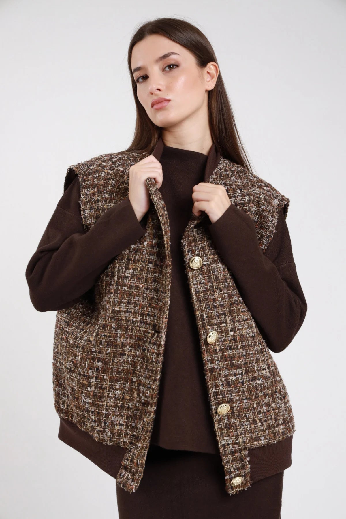 Bomber gilet smanicato tweed bouclé marrone oro beige bottoni dorati gioiello spallina squadrata sfrangiata girocollo tondo fondo coste elasticizzato boxy frontale tre quarti mano fianco - modella frontale tre quarti mano fianco sguardo laterale capelli castani lisci lunghi sfondo bianco maglia marrone gonna marrone