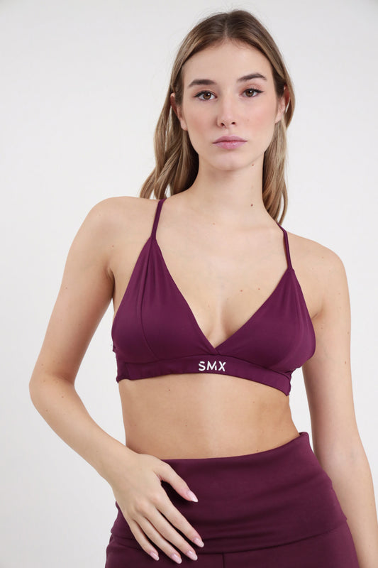 Bralette SMX Limited Edition bordeaux prugna 95% tactel triangolo scollo V spalline incrociate cross-back fascia elastica logo SMX bianco crop frontale busto mani fianco - modella busto frontale mani fianco sguardo frontale capelli raccolti sfondo bianco pantalone gonna bordeaux coordinato abbinato