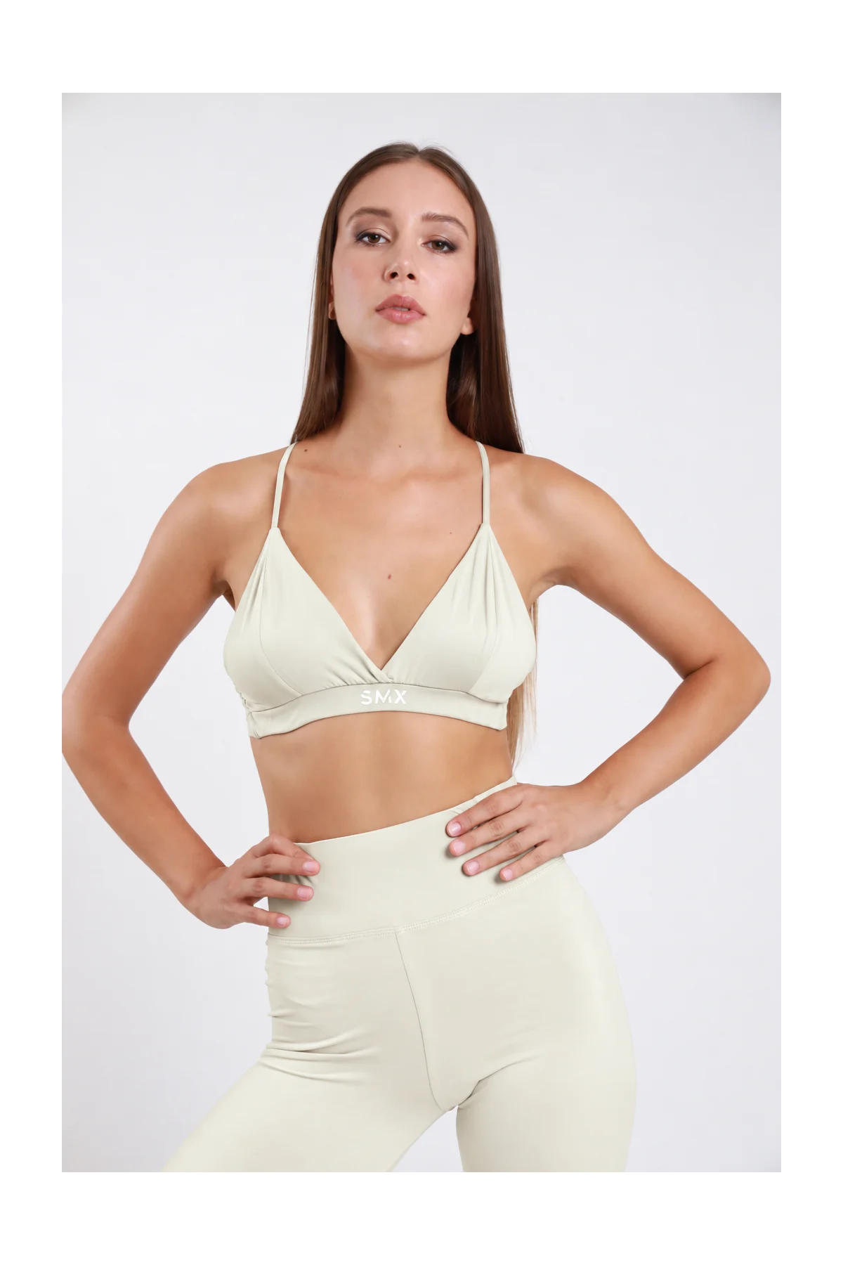 Bralette Triangolo DAYTHRU panna avorio scollo V profondo incrociato spalline sottili fascia elastica logo SMX bianco centrato second-skin busto frontale posa statica mani fianchi sguardo frontale - modella busto frontale posa statica mani fianchi sguardo frontale capelli castani lisci sfondo bianco leggings panna avorio coordinati