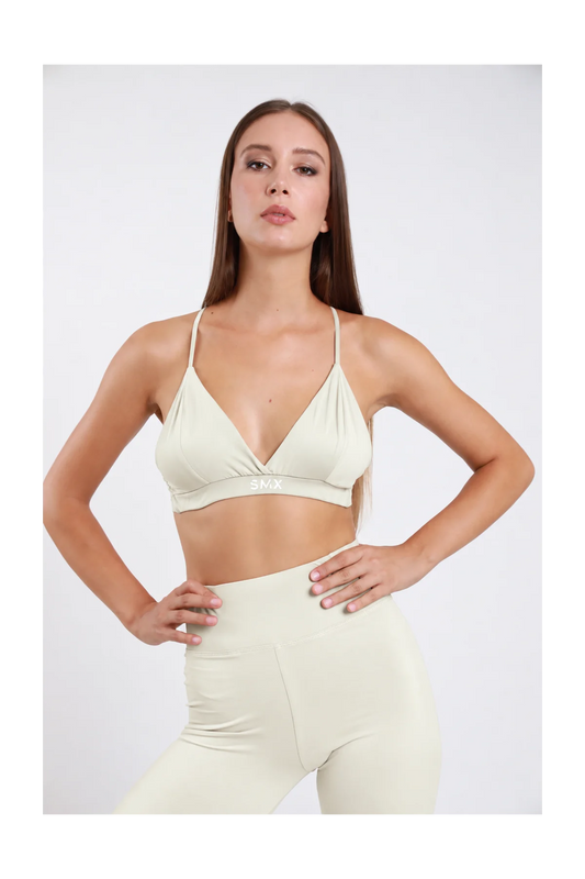 Bralette Triangolo DAYTHRU panna avorio scollo V profondo incrociato spalline sottili fascia elastica logo SMX bianco centrato second-skin busto frontale posa statica mani fianchi sguardo frontale - modella busto frontale posa statica mani fianchi sguardo frontale capelli castani lisci sfondo bianco leggings panna avorio coordinati