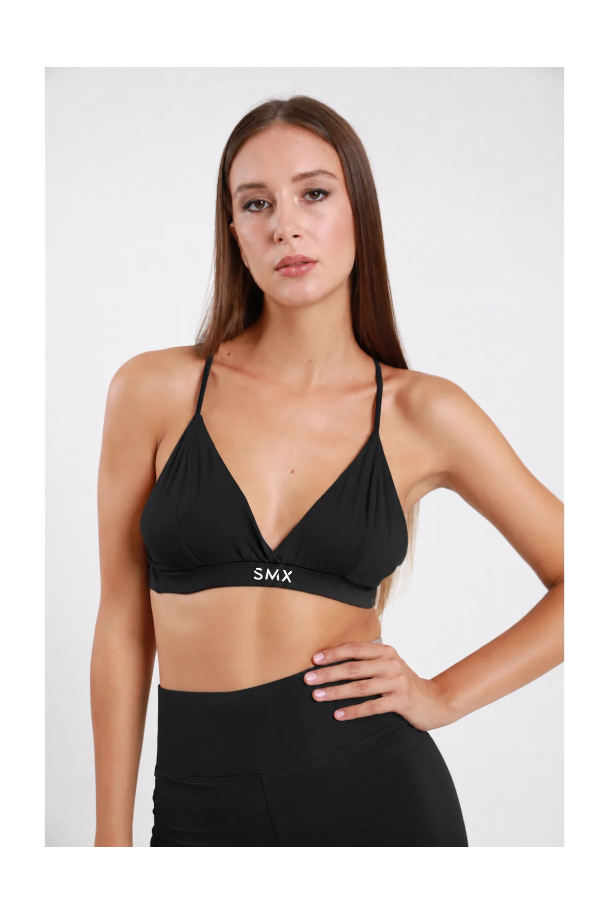 Bralette Triangolo DAYTHRU nero scollo V profondo incrociato spalline sottili fascia elastica logo SMX bianco a contrasto second-skin busto frontale posa statica mano fianco sguardo frontale - modella busto frontale posa statica mano fianco sguardo frontale capelli castani lisci sfondo bianco leggings neri coordinati