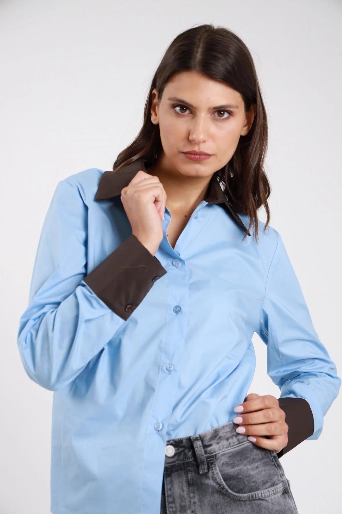 Camicia bicolor 100% cotone azzurro celeste corpo marrone cioccolato colletto polsini contrasto balloon oversize relaxed frontale busto mano pugno colletto - modella frontale busto mano pugno colletto sguardo laterale capelli castani scuri ondulati sfondo bianco jeans grigio