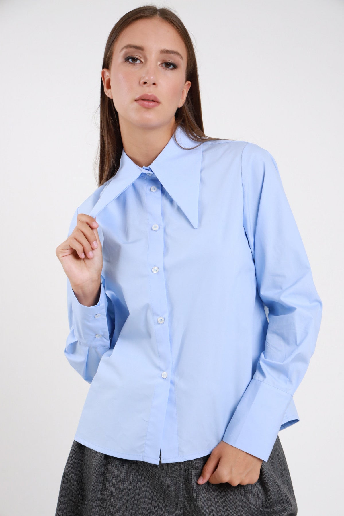Camicia Oversize Maxi Colletto Appuntito azzurro celeste 100% cotone popeline maxi colletto punta lunga strutturato ben visibile bottoni bianchi chiusura frontale polsino bottone - modella busto frontale 3/4 posa mano colletto sguardo frontale capelli castani lisci sfondo bianco