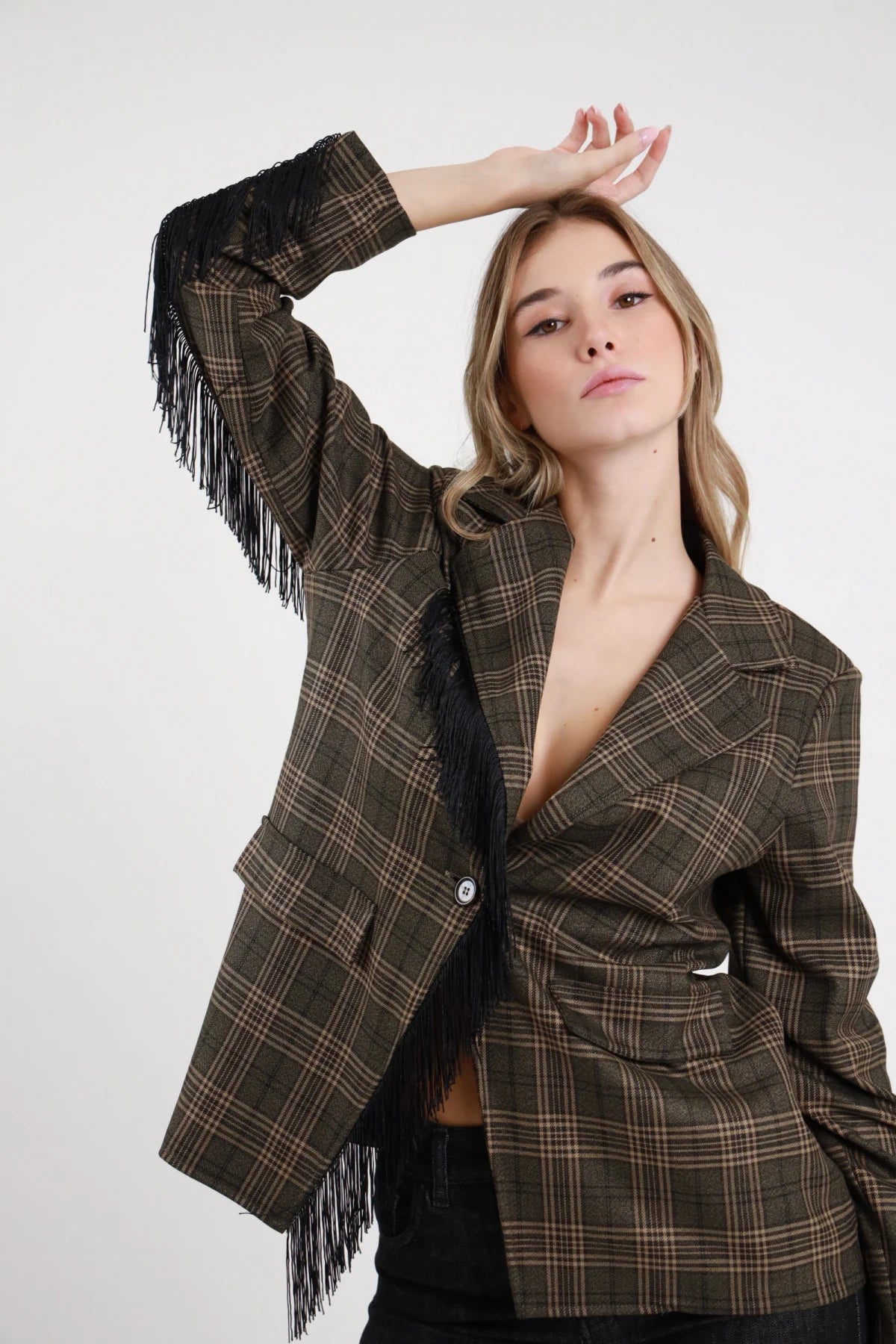 Blazer Check Frange verde militare check Glen plaid frange nere fluenti dinamiche bordo manica molto vistose dettaglio busto braccio alzato posa dinamica - modella busto 3/4 braccio alzato sguardo frontale intenso capelli biondi mossi sfondo bianco jeans nero slim abbinati