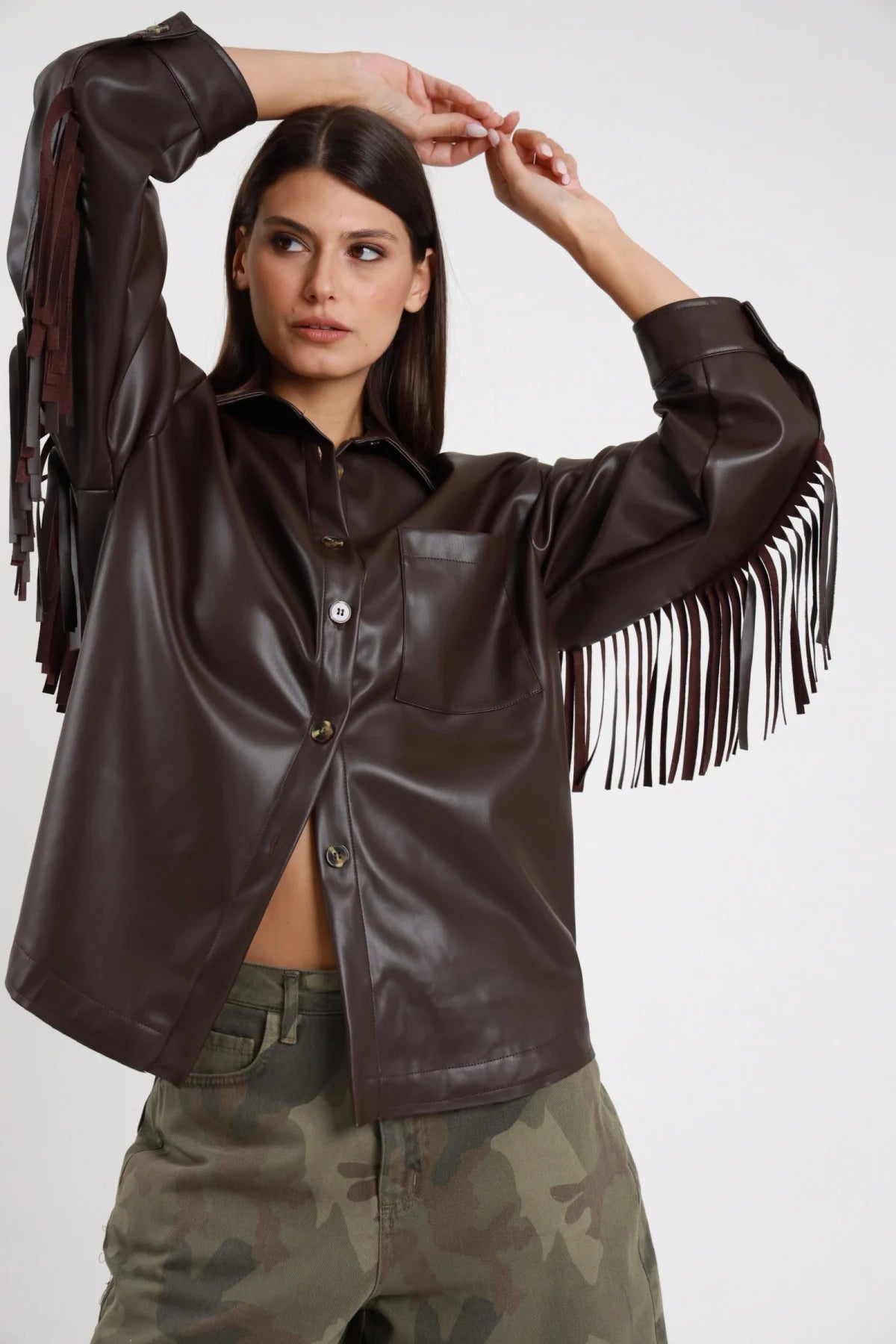 Camicia Ecopelle Frange marrone cioccolato testa di moro 50% PU colletto classico rovesciato bottoni bruniti antichi tasca petto manica balloon frange lunghe tutta manica silhouette oversize boxy frontale braccia alzate - modella busto frontale braccia alzate mani testa sguardo laterale capelli castani scuri sfondo bianco bermuda mimetico woodland