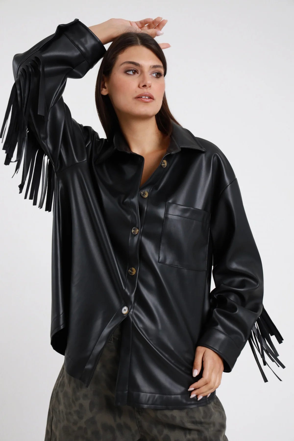 Camicia Ecopelle Frange nero lucido 50% PU colletto classico rovesciato bottoni dorati bronzo tasca petto manica balloon frange lunghe tutta manica silhouette oversize boxy frontale braccia alzate - modella busto frontale braccia alzate mano testa sguardo laterale capelli castani scuri sfondo bianco pantaloni leopardati mimetico scuro
