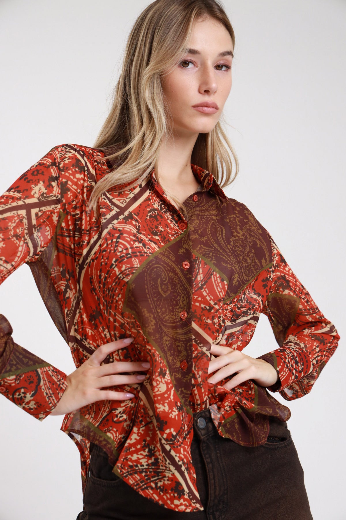Camicia fantasia paisley cachemire rosso borgogna cioccolato frontale mani fianchi colletto bottoni placchetta manica lunga - modella frontale intera mani fianchi sguardo frontale pantaloni marrone scuro capelli biondi ondulati