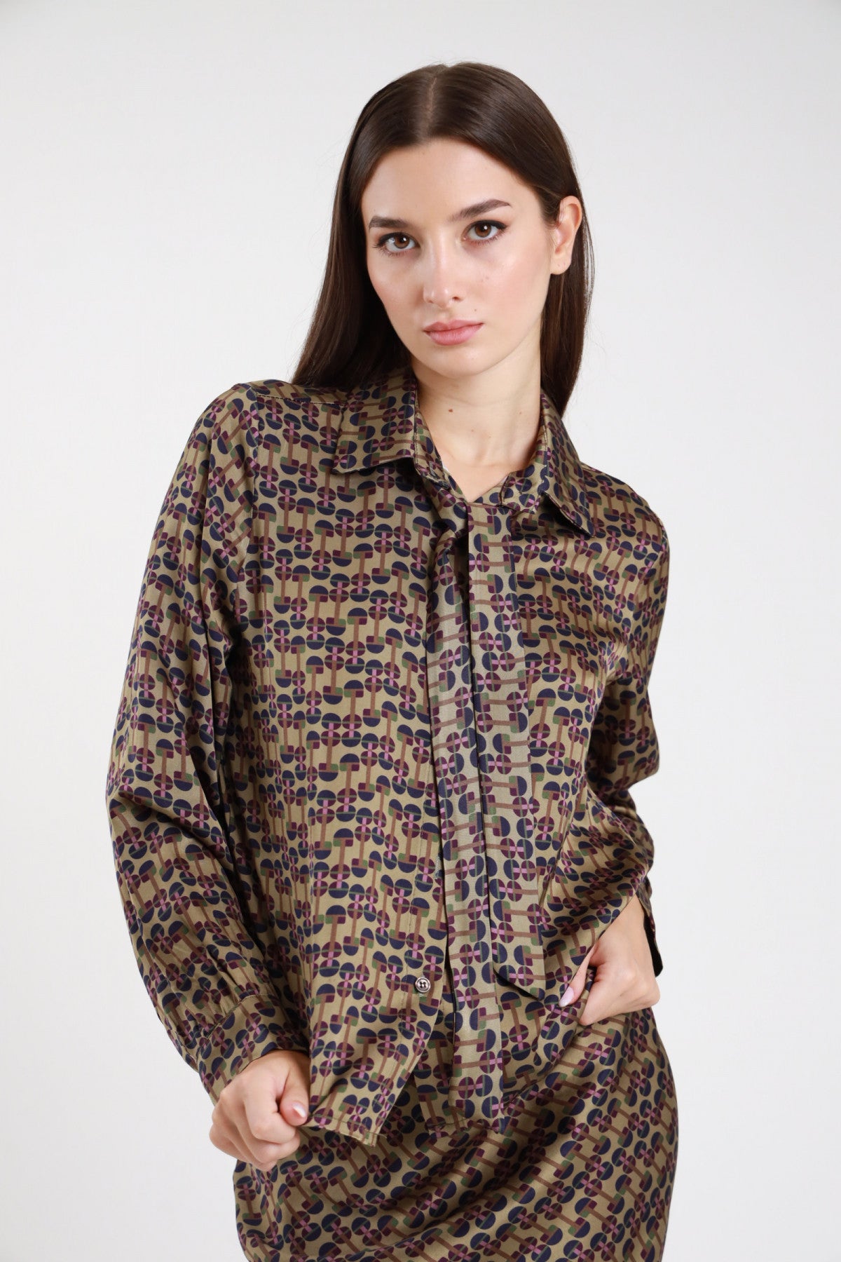 Camicia fantasia geometrica retro anni 70 cachi marrone viola donna oversize satinata viscosa colletto classico bottoni cravattino lavallière maniche lunghe polsino - vista frontale mezzo busto mani in tasca con pantaloni coordinati