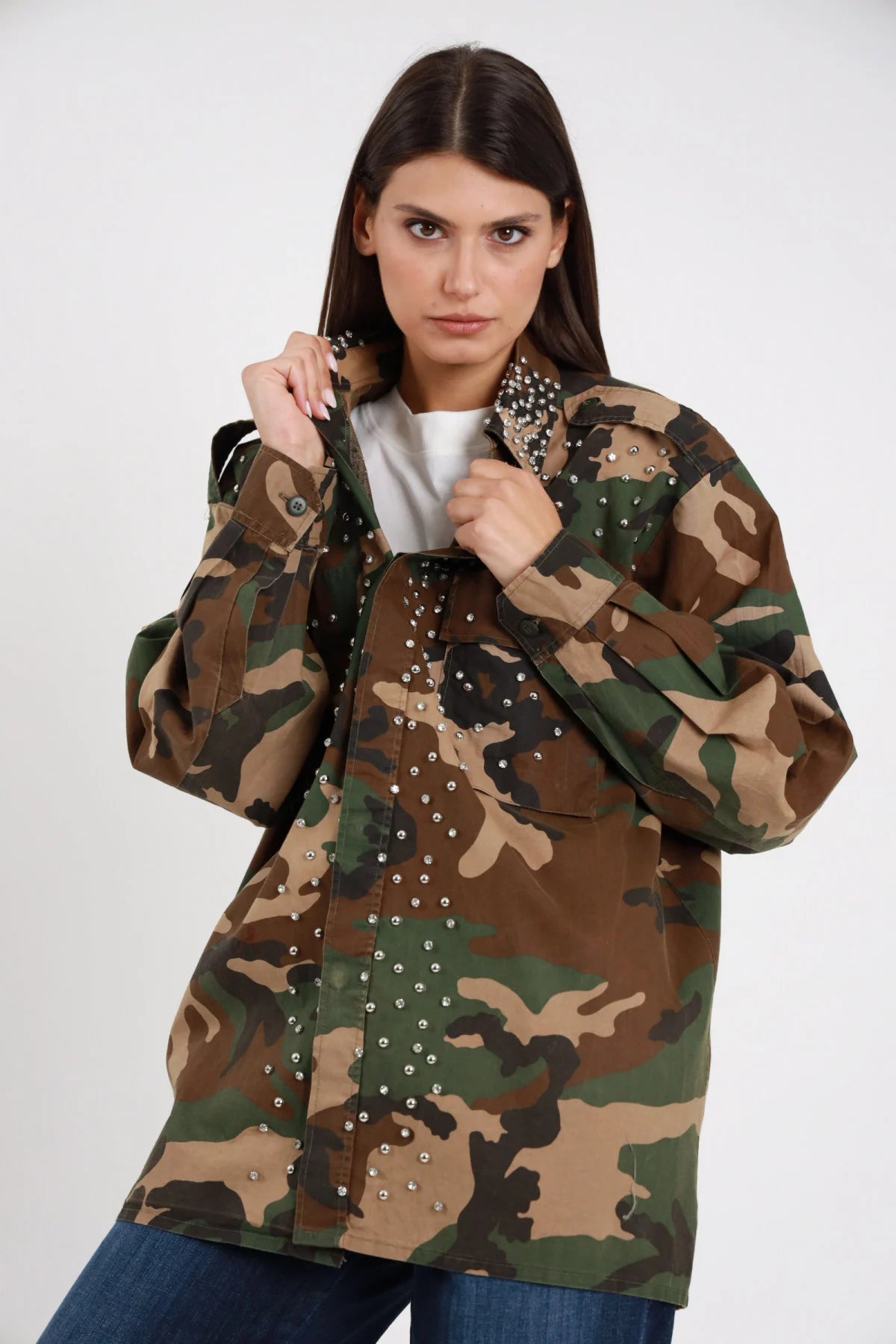 Camicia Militare Mimetica Woodland Borchie Strass 95% cotone colletto militare ricoperto borchie strass argentati applicazioni strass pioggia petto davanti tasche chiusura bottoni silhouette oversize lunga maxi - modella busto 3/4 frontale posa mani colletto rialzato sguardo frontale intensissimo make-up bold capelli castani lisci sfondo bianco