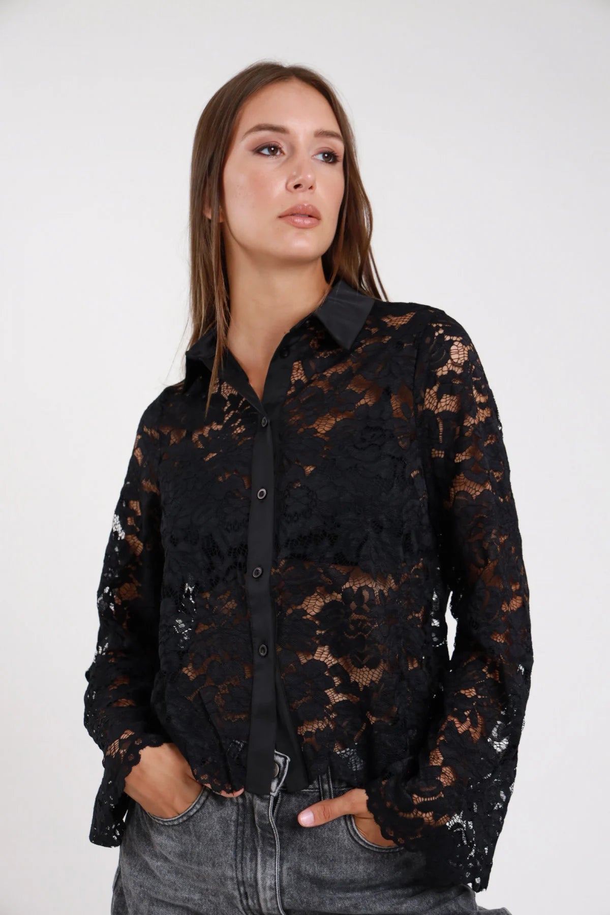 Camicia pizzo nero semitrasparente frontale busto mani tasche jeans grigio colletto classico punta abbottonatura bottoni neri manica lunga pizzo floreale maxi - modella frontale busto mani tasche sguardo frontale jeans grigio capelli castani lisci sciolti