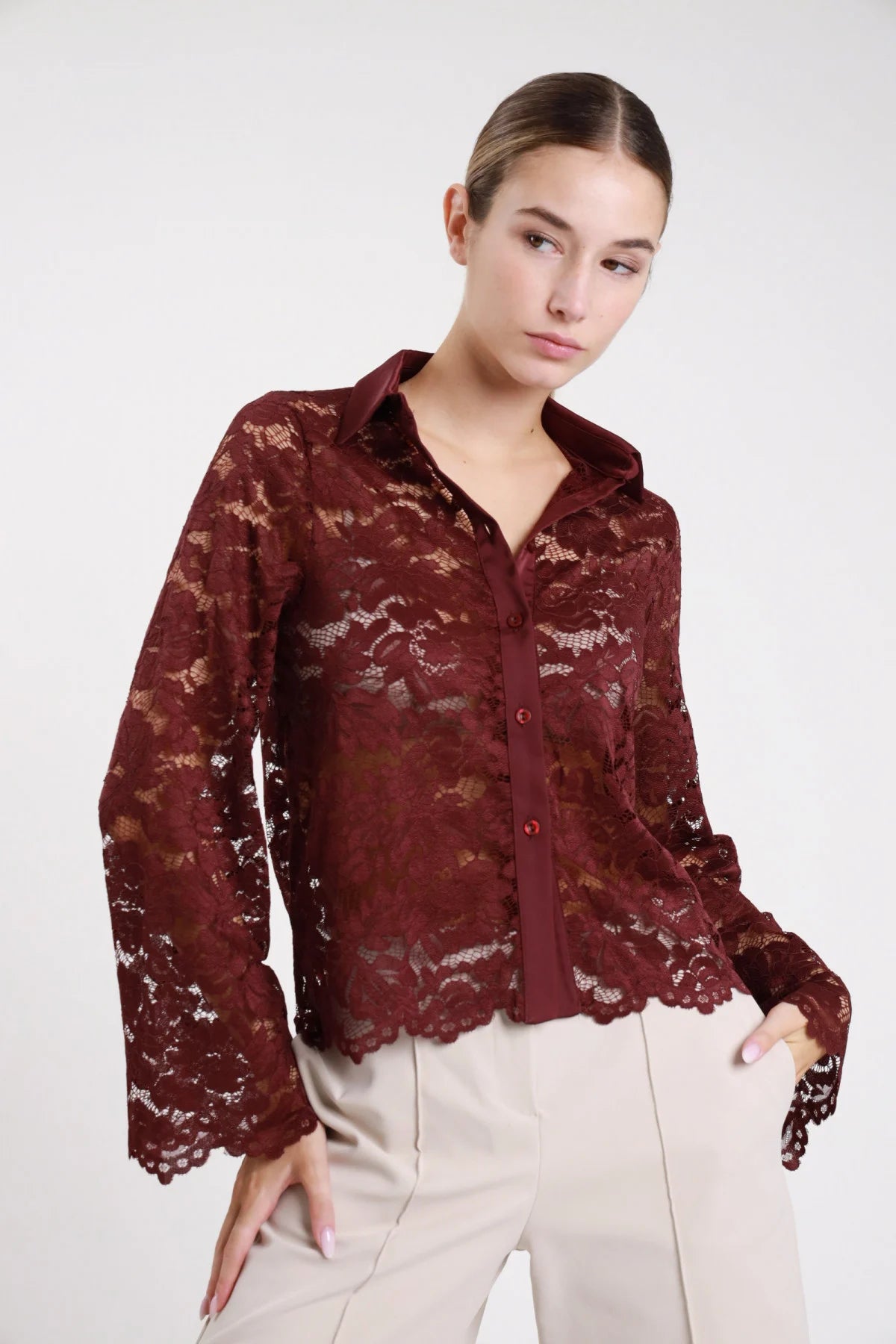 Camicia pizzo bordeaux marsala vino semitrasparente frontale intera mani tasche manica campana flare orlo scallop smerlato floreale abbottonatura bottoni bordeaux corpo relaxed - modella frontale intera mani tasche sguardo frontale pantaloni beige capelli castani raccolti bun