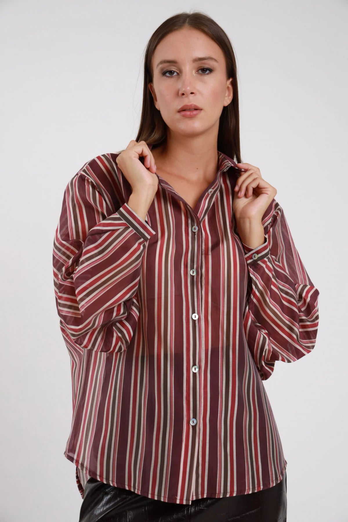 Camicia Righe verticali multicolore bordeaux verde beige rosso oversize batwing colletto classico bottoni madreperlacei busto frontale 3/4 mani colletto - modella busto frontale 3/4 mani colletto sguardo frontale capelli castani lisci sfondo bianco pantalone nero ecopelle