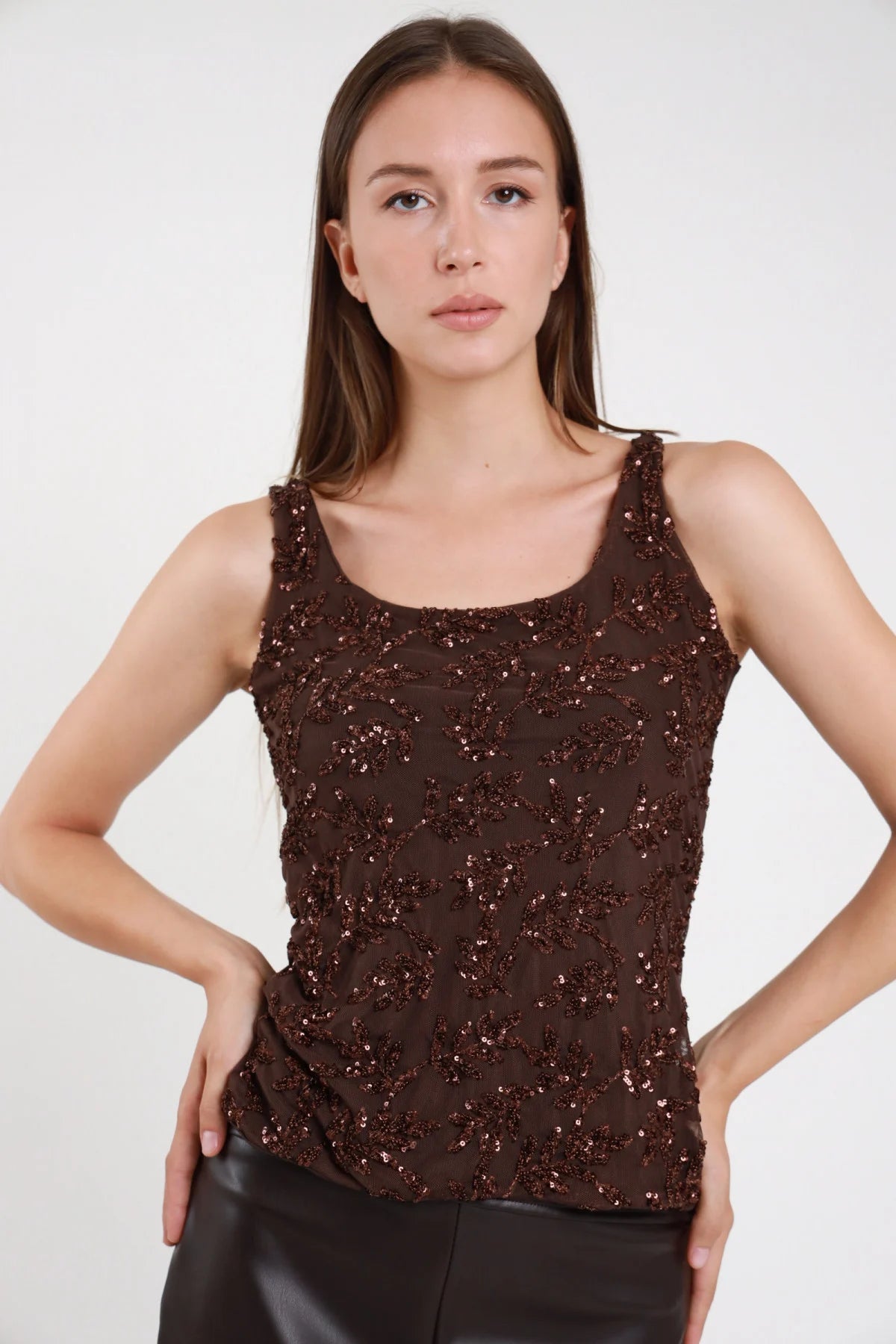 Top paillettes marrone cioccolato donna scollo tondo spalline larghe motivo floreale ramoscelli - vista frontale mani sui fianchi pantaloni in ecopelle neri