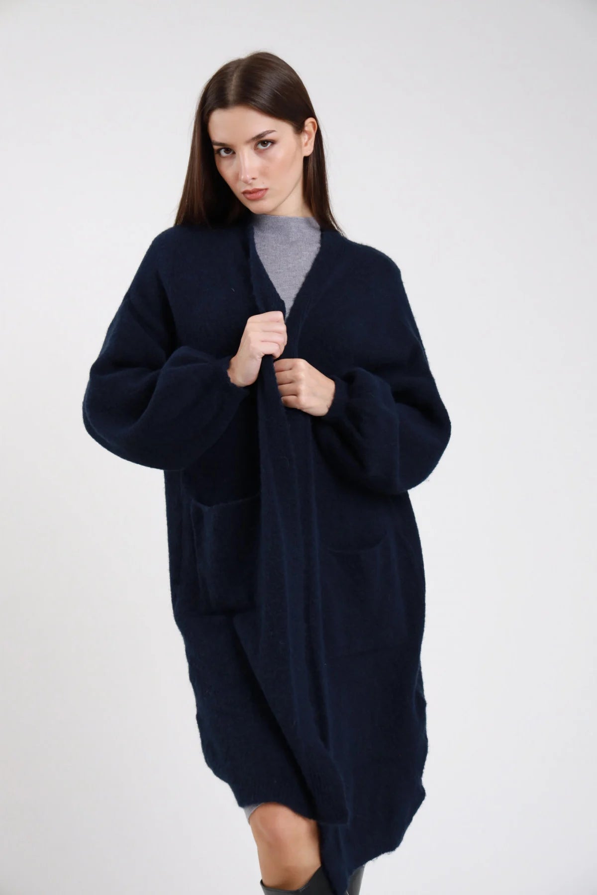 Cardigan lungo midi maglia bouclé eyelash blu navy notte aperto scollo V revers batwing oversize cocoon tasche patch frontale tre quarti mani risvolto - modella frontale tre quarti mani risvolto sguardo frontale capelli castani scuri lisci sfondo bianco stivali neri maglia grigio turtleneck